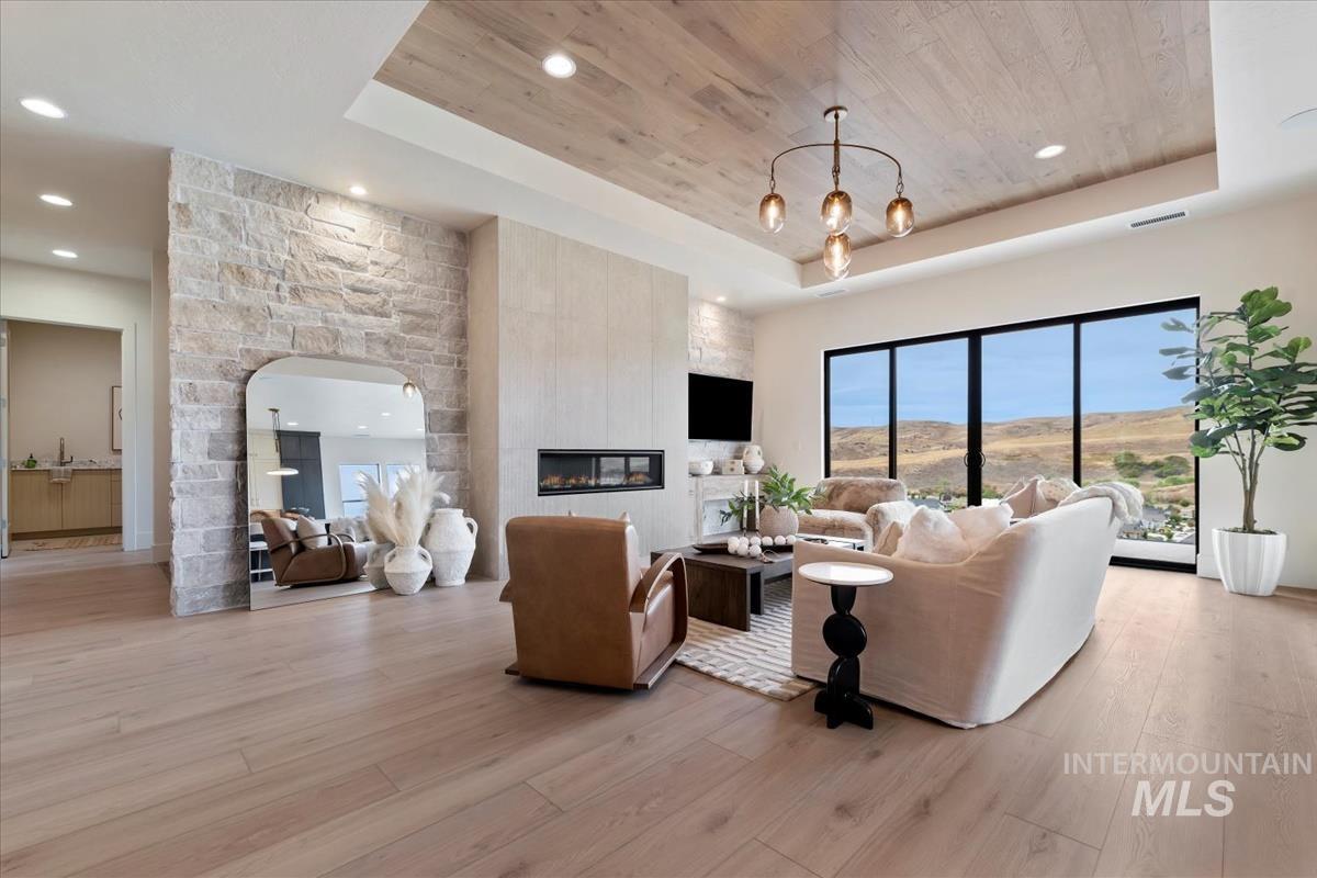 Living area featuring a tray ceiling, recessed lighting, light wood-style flooring, wooden ceiling, and a fireplace