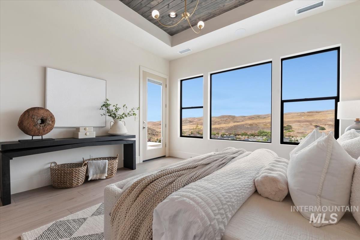 Bedroom with a tray ceiling, wood finished floors, access to exterior, wooden ceiling, and a chandelier