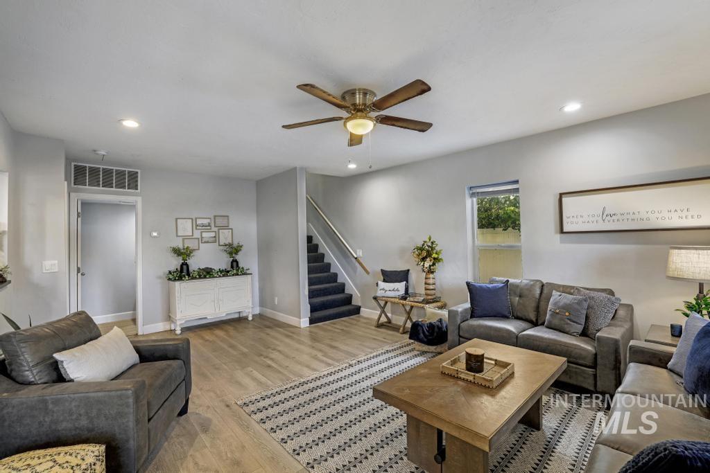 Living room with light wood-type flooring, recessed lighting, a ceiling fan, and stairs
