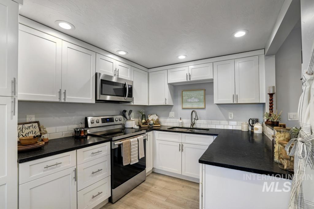 Kitchen with appliances with stainless steel finishes, white cabinetry, light wood finished floors, recessed lighting, and dark stone counters