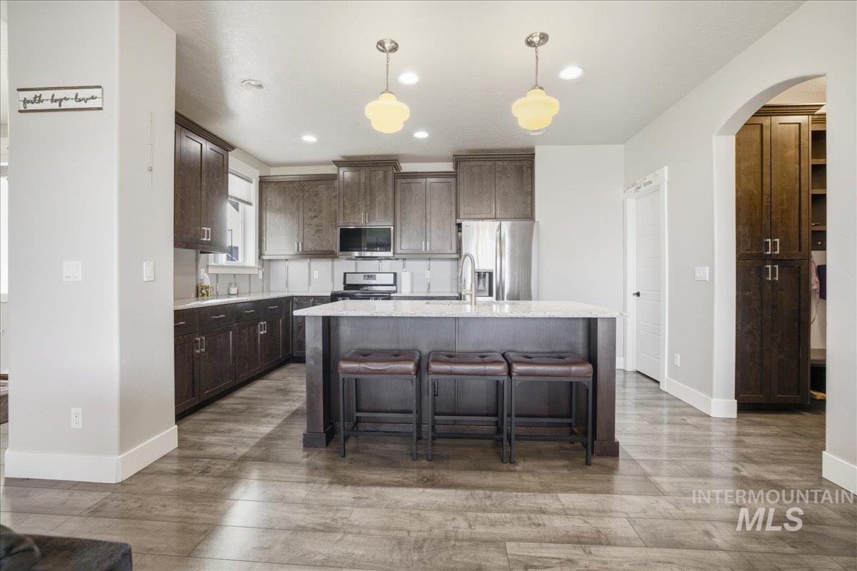 Kitchen featuring arched walkways, dark brown cabinets, appliances with stainless steel finishes, pendant lighting, and a kitchen bar