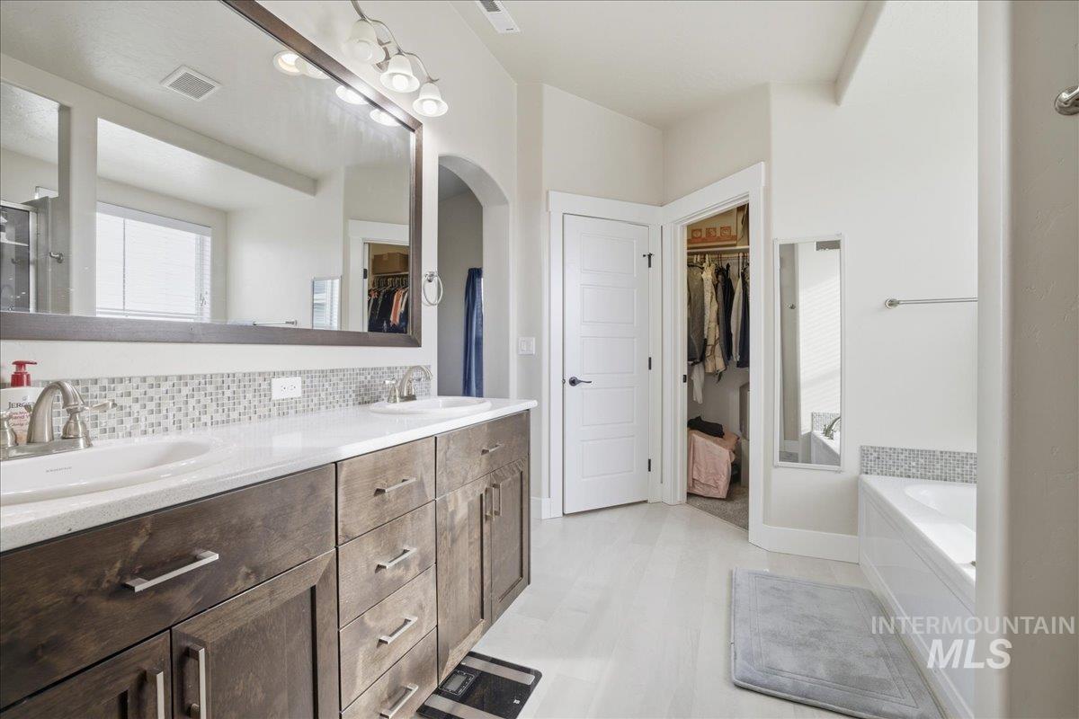 Bathroom featuring a walk in closet, double vanity, a garden tub, and tasteful backsplash