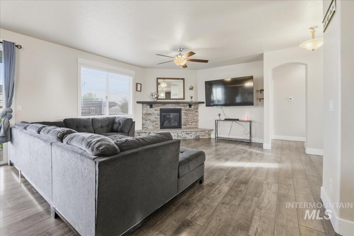 Living room with a fireplace, arched walkways, wood finished floors, a ceiling fan, and a textured ceiling