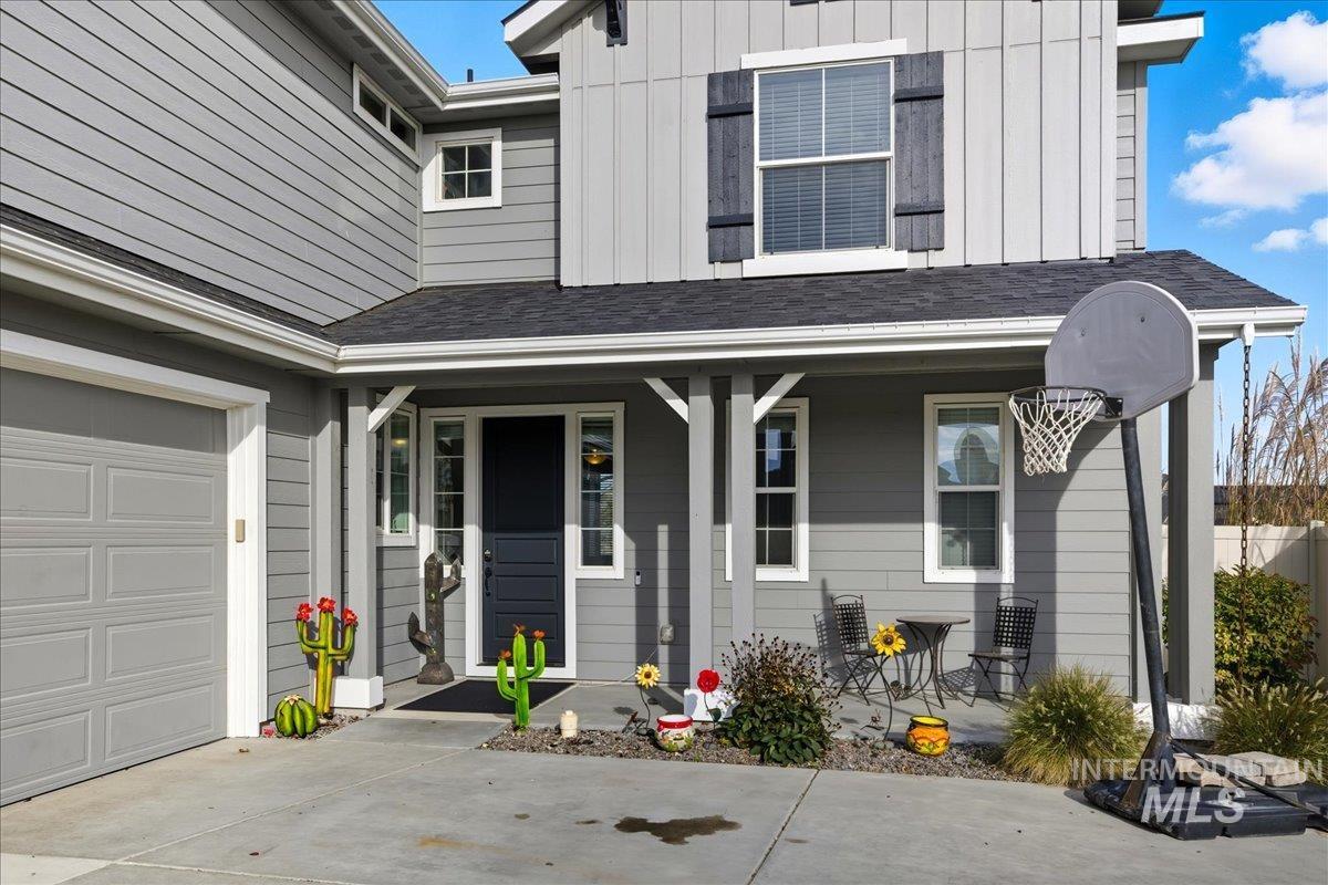 Property entrance with board and batten siding, a porch, roof with shingles, and driveway
