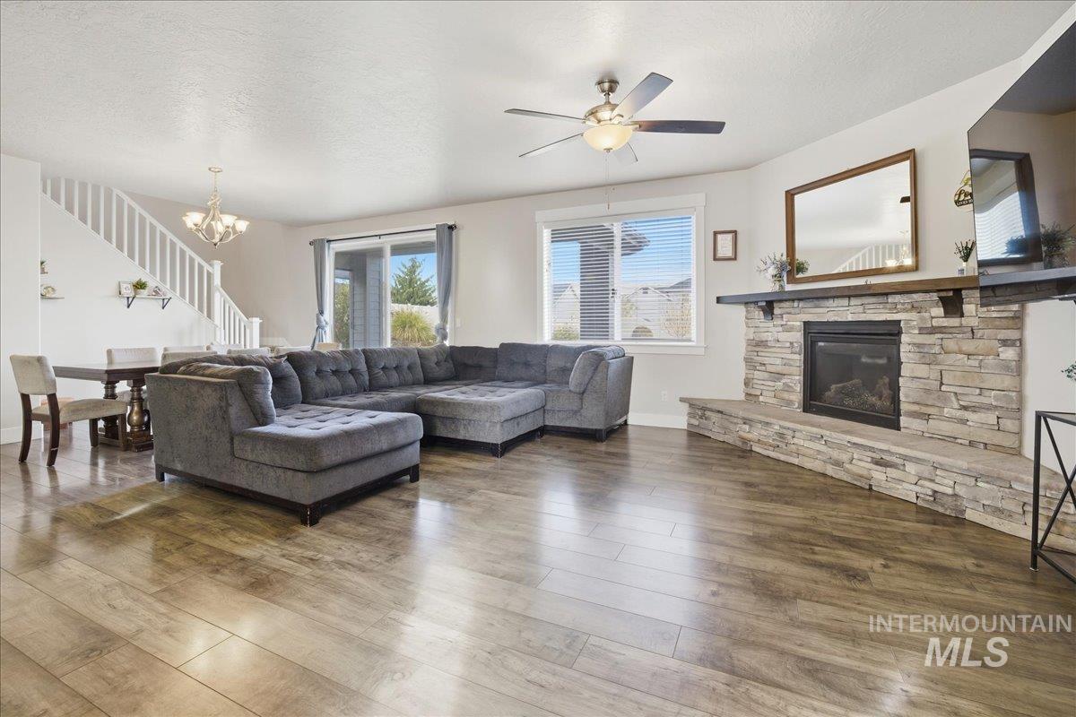 Living room featuring a textured ceiling, wood finished floors, a stone fireplace, a chandelier, and ceiling fan