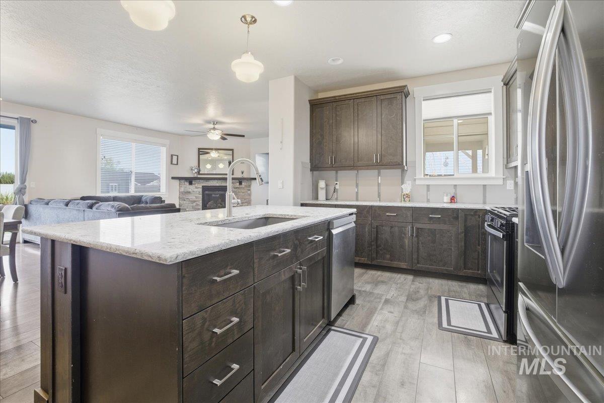 Kitchen with stainless steel appliances, dark brown cabinets, light wood-style flooring, open floor plan, and a stone fireplace