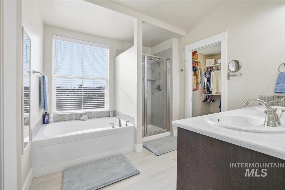 Bathroom featuring a shower stall, a garden tub, vanity, a walk in closet, and light wood-style flooring
