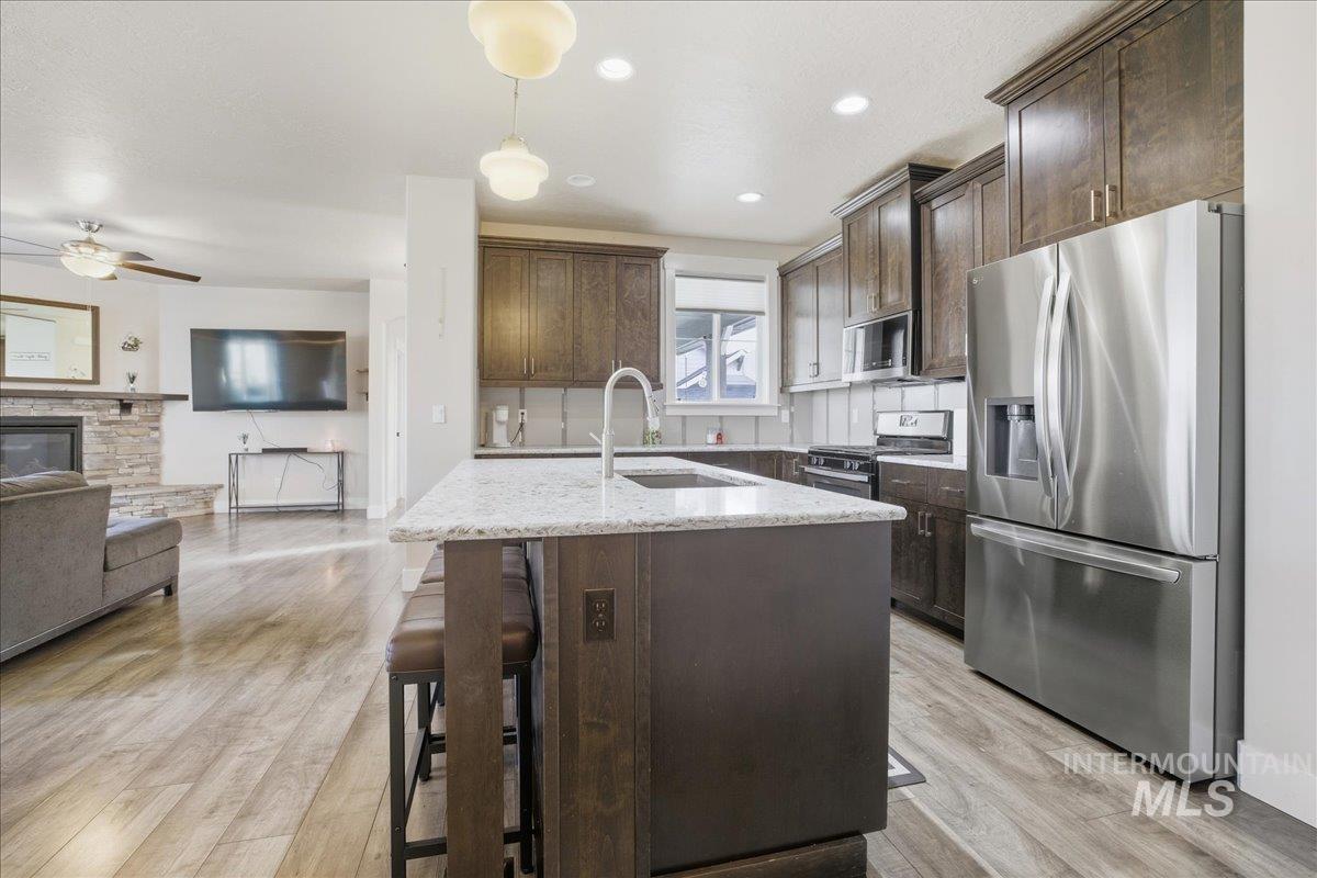 Kitchen with appliances with stainless steel finishes, light stone counters, pendant lighting, dark brown cabinets, and recessed lighting