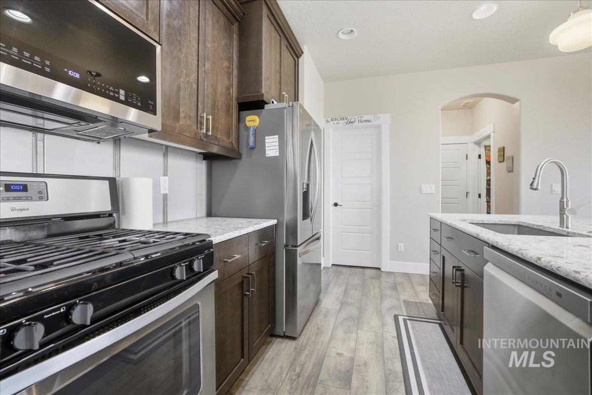 Kitchen with appliances with stainless steel finishes, light stone counters, light wood-style floors, dark brown cabinetry, and recessed lighting