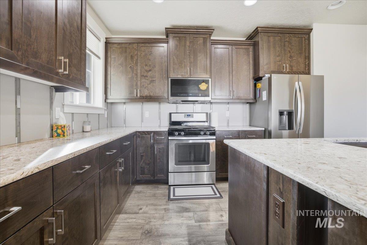 Kitchen featuring dark brown cabinetry, stainless steel appliances, light wood finished floors, light stone counters, and recessed lighting