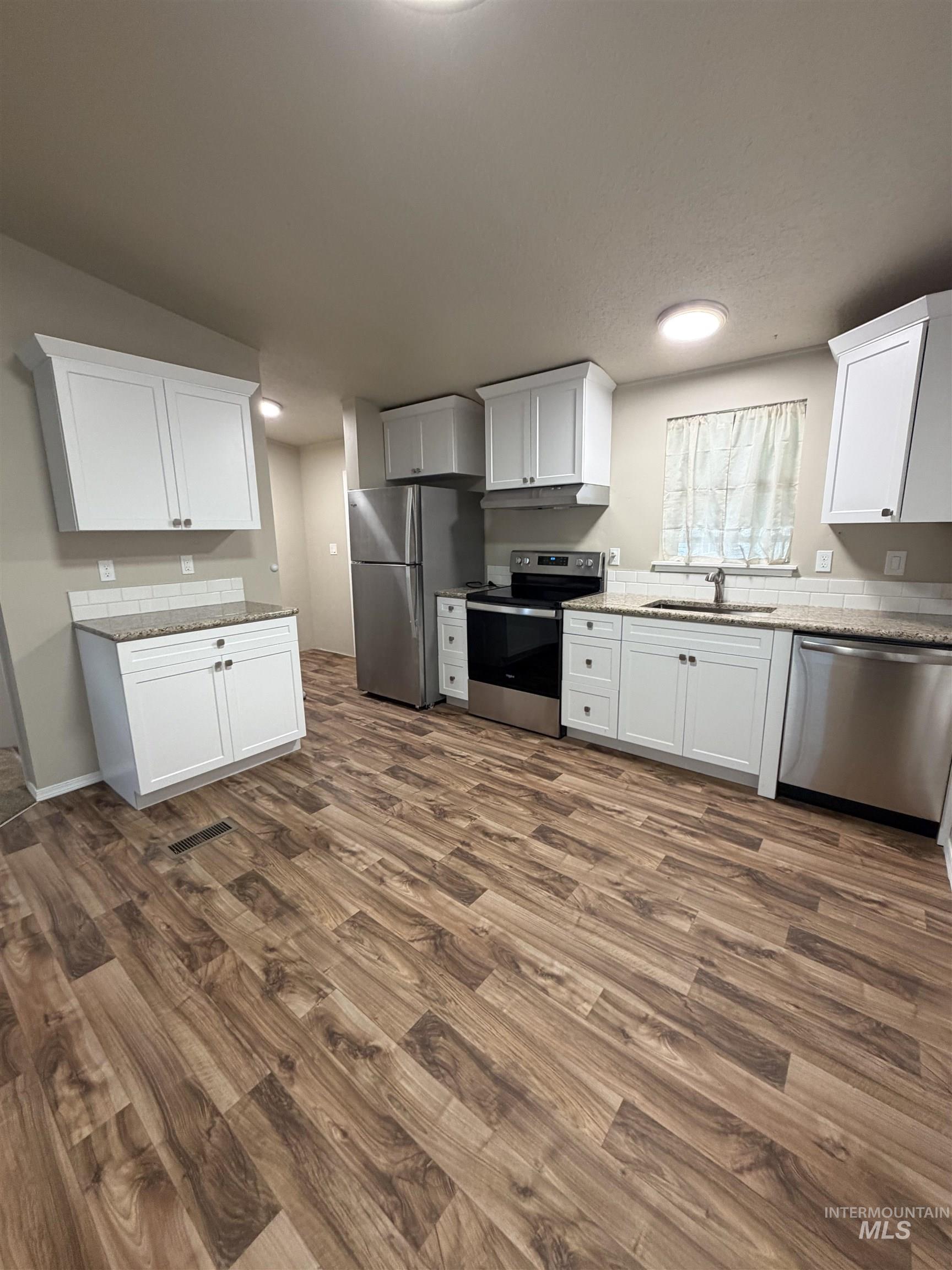 Kitchen featuring stainless steel appliances, white cabinetry, dark wood-style flooring, and light stone countertops