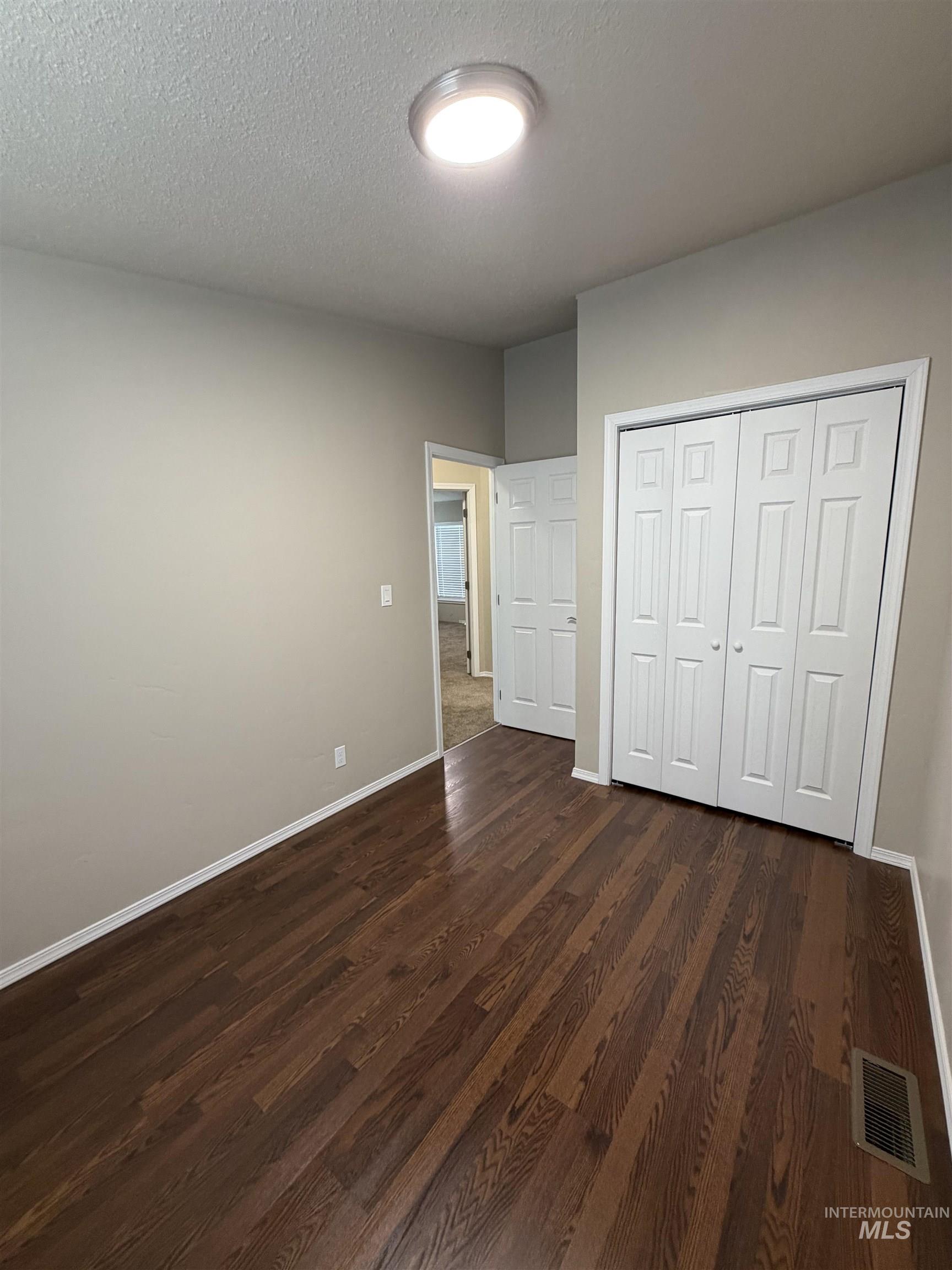 Unfurnished bedroom with dark wood-type flooring, a closet, and a textured ceiling