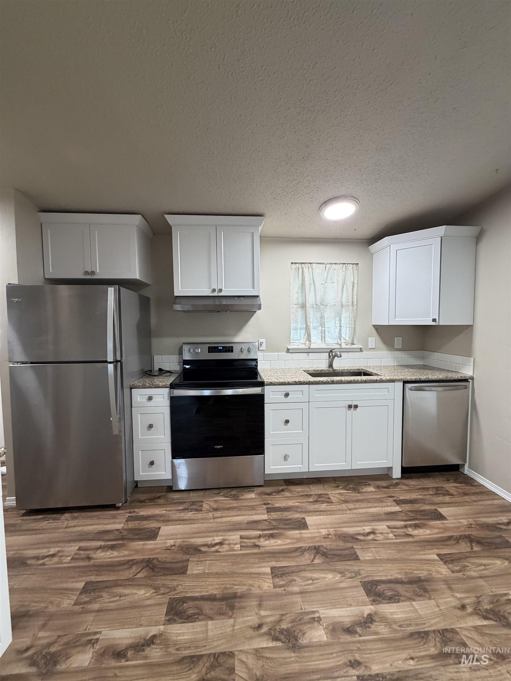 Kitchen featuring stainless steel appliances, white cabinetry, light stone counters, dark wood-style flooring, and a textured ceiling