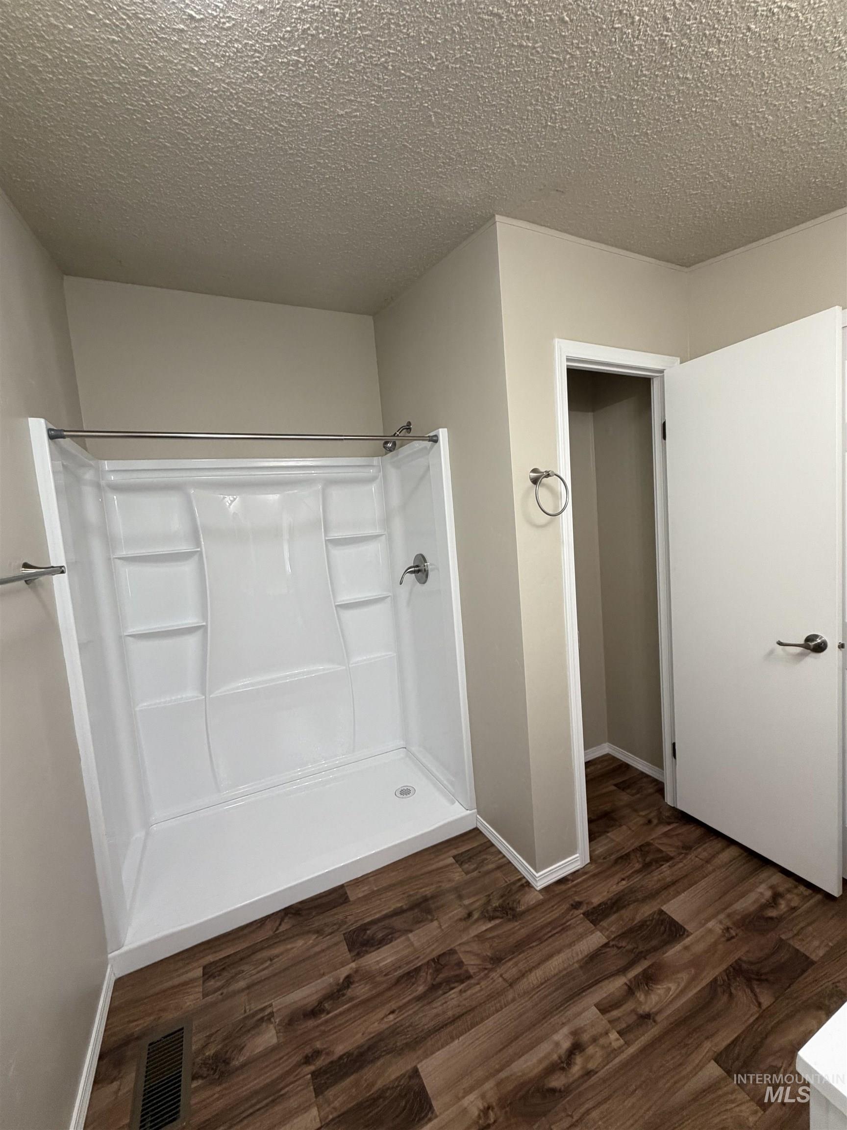 Bathroom with a shower stall, a textured ceiling, and dark wood finished floors
