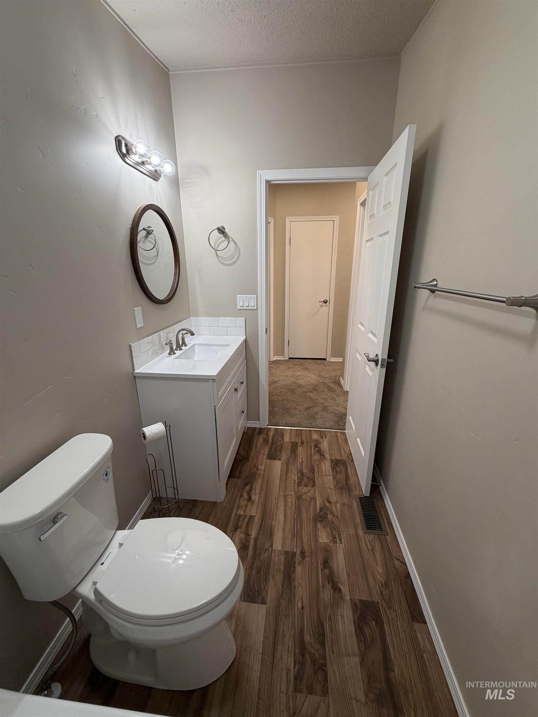 Half bath with dark wood finished floors, vanity, and a textured ceiling