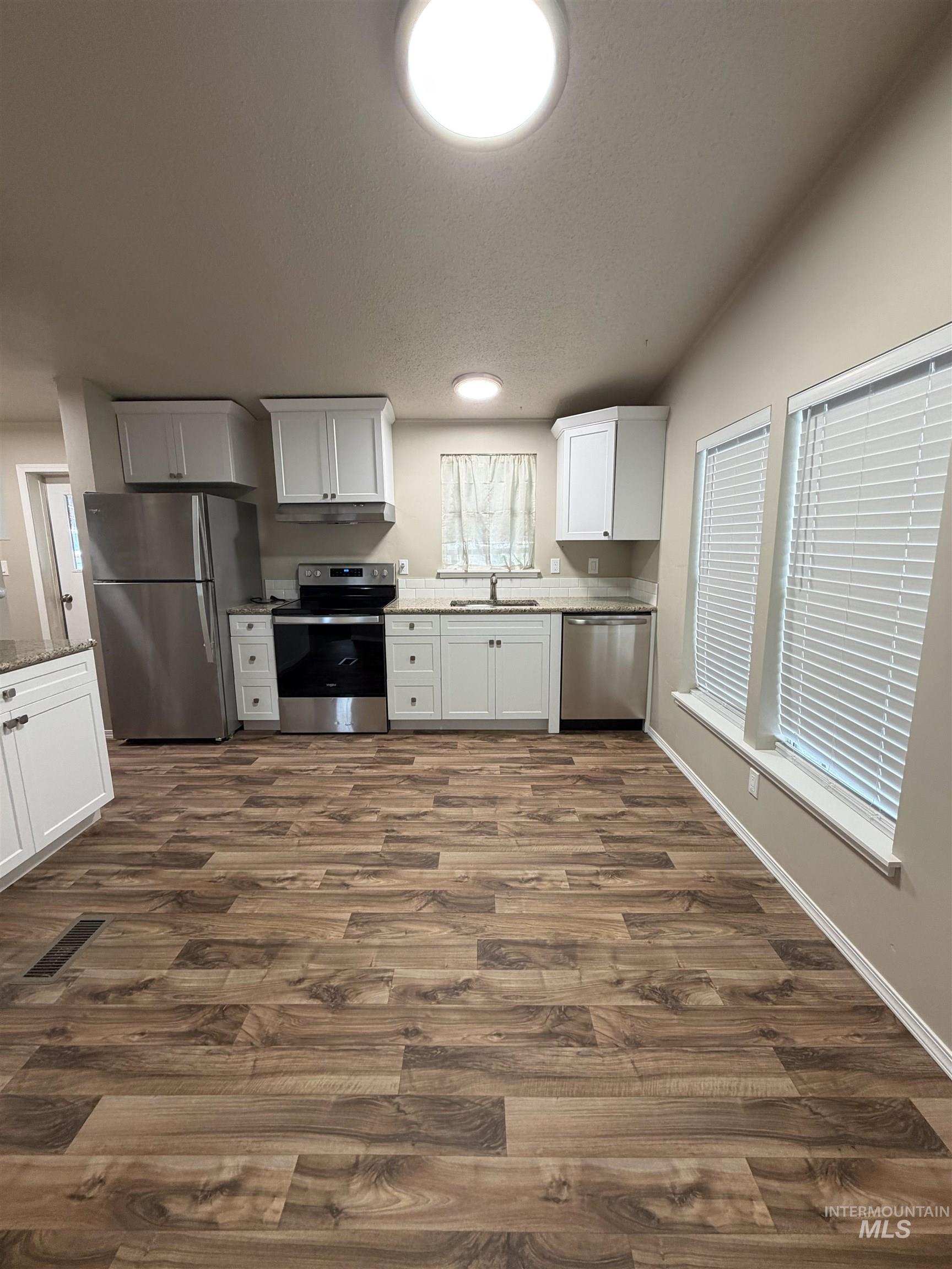 Kitchen featuring stainless steel appliances, white cabinets, light stone countertops, dark wood-style floors, and a textured ceiling