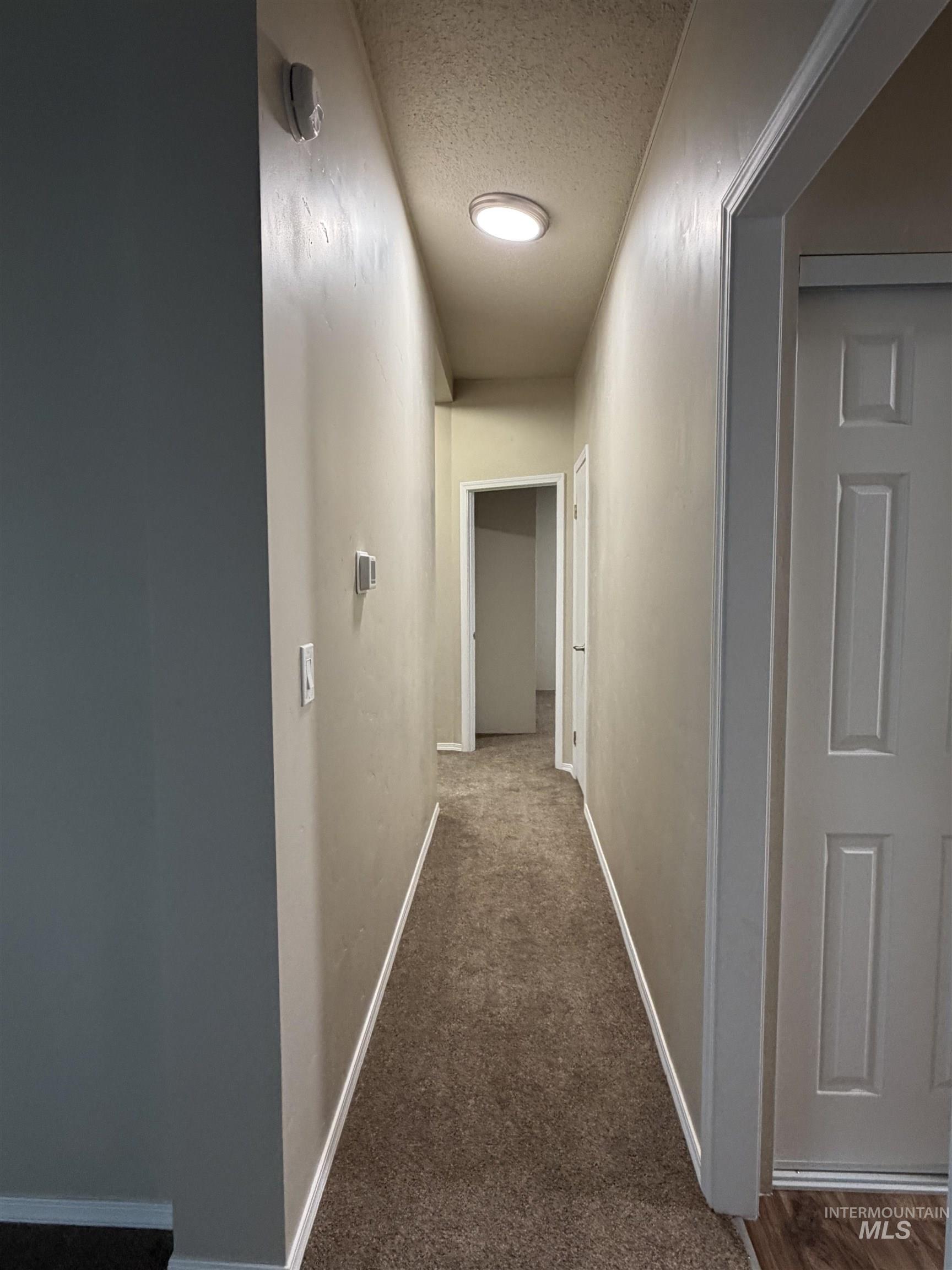 Hallway featuring dark colored carpet and a textured ceiling