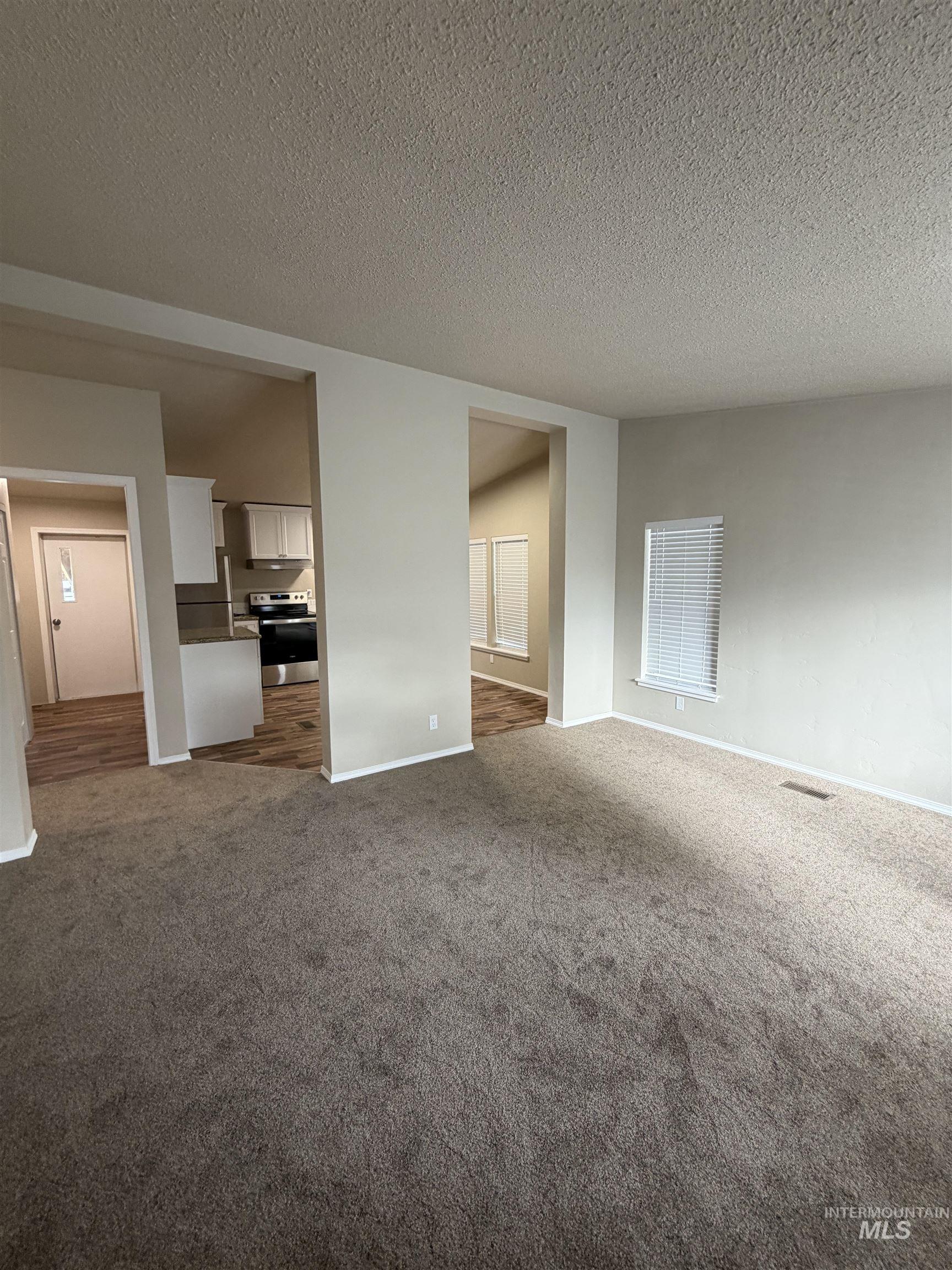 Unfurnished living room featuring a textured ceiling and dark colored carpet