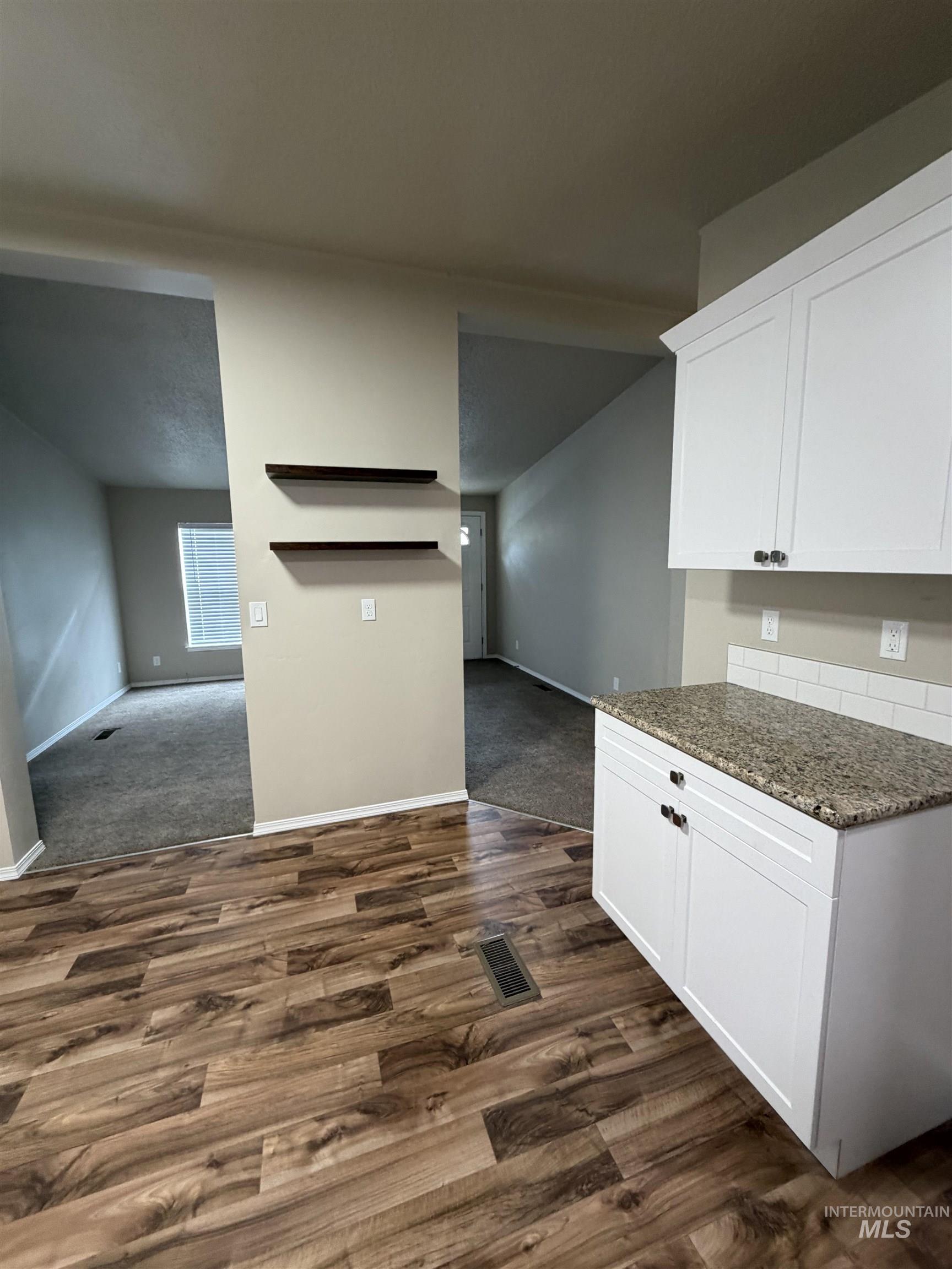 Kitchen featuring dark stone countertops, white cabinets, dark wood-style flooring, dark colored carpet, and open floor plan