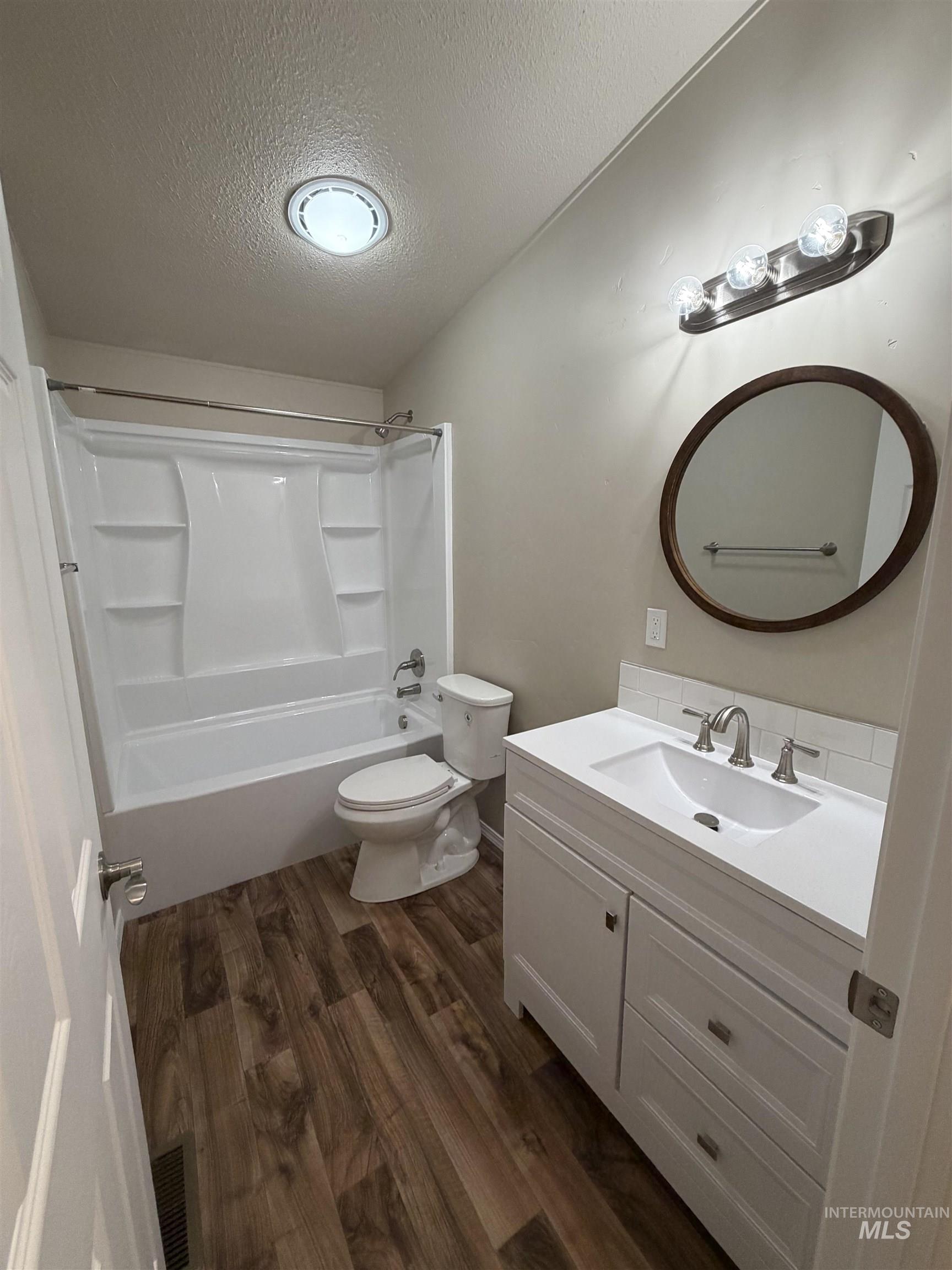 Bathroom with vanity, dark wood finished floors, bathtub / shower combination, and a textured ceiling