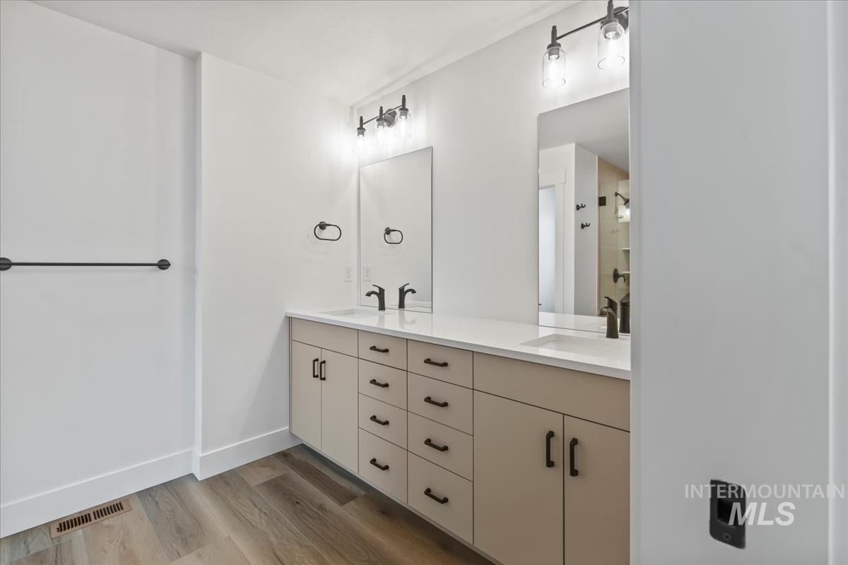 Bathroom with light wood-style flooring, double vanity, and tiled shower