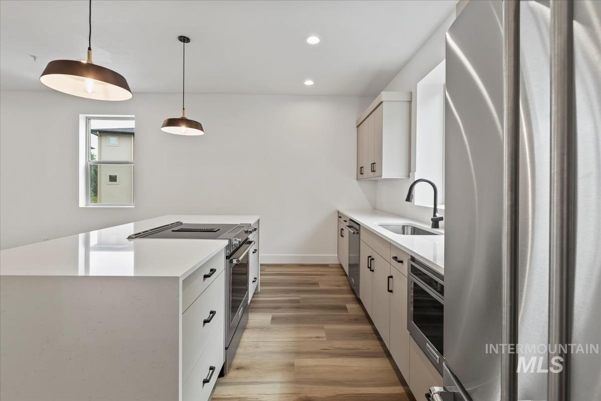Kitchen with stainless steel appliances, light stone countertops, pendant lighting, light wood-style floors, and recessed lighting
