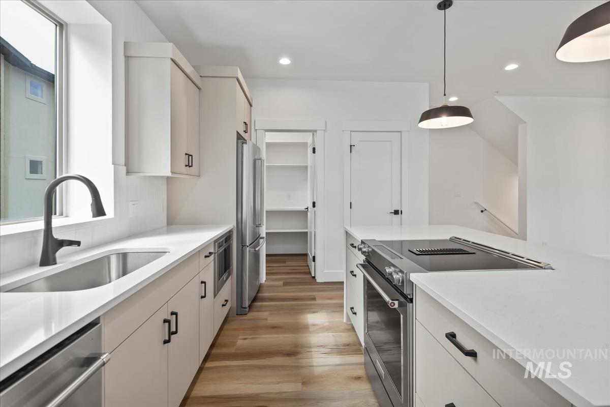 Kitchen featuring stainless steel appliances, pendant lighting, light wood-style flooring, light stone counters, and recessed lighting