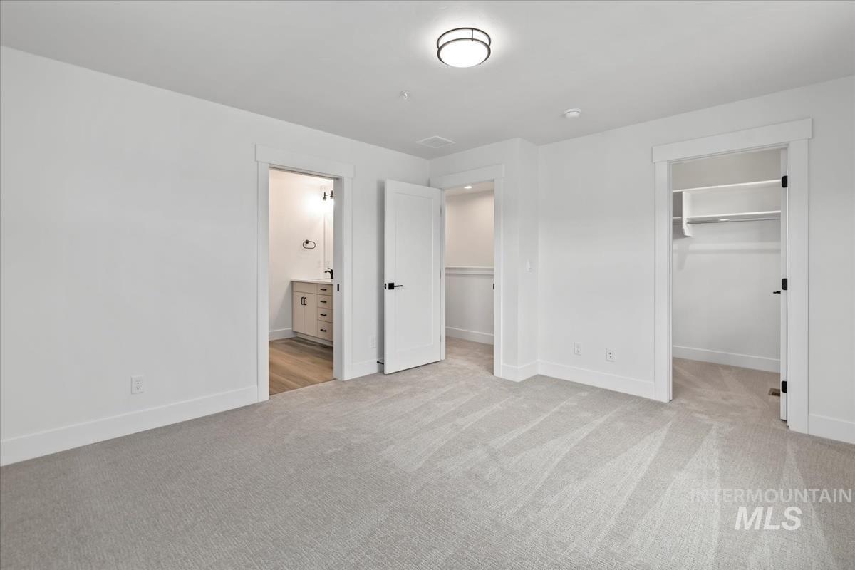 Unfurnished bedroom with a spacious closet, light carpet, and ensuite bathroom