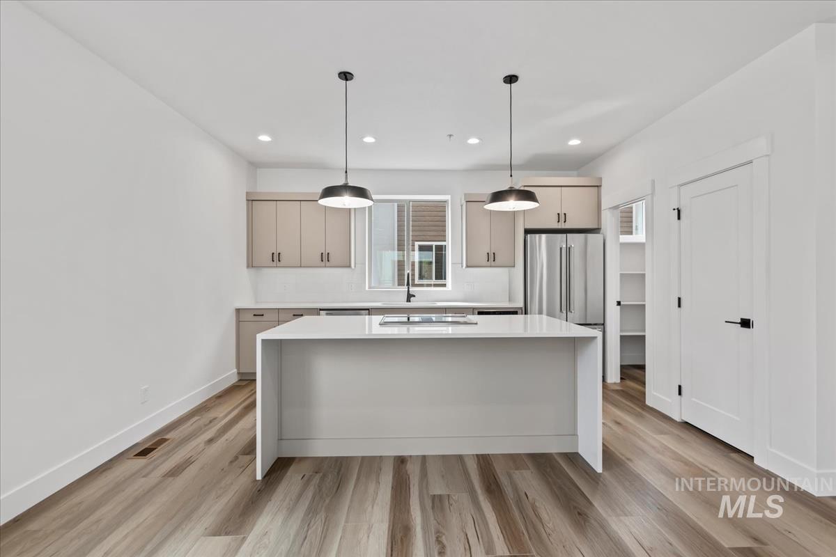 Kitchen with a kitchen island, pendant lighting, light stone counters, light wood-type flooring, and recessed lighting