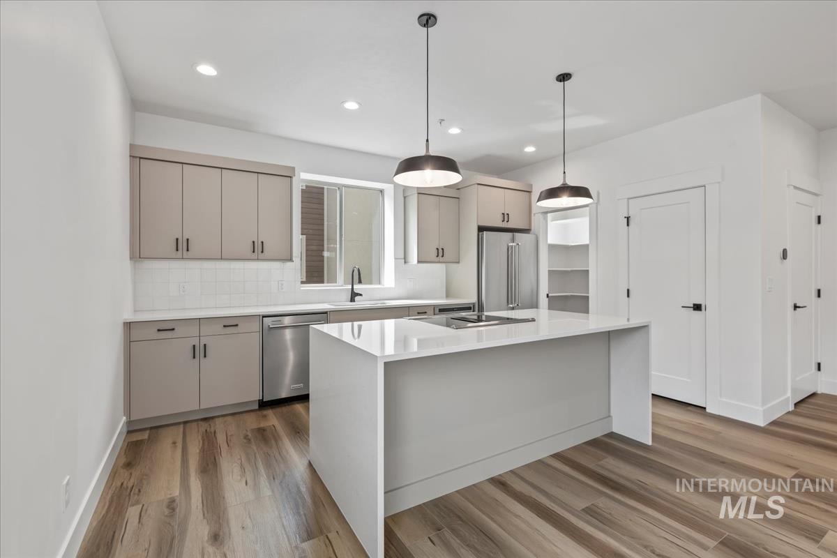 Kitchen with hanging light fixtures, decorative backsplash, light stone counters, stainless steel appliances, and gray cabinets
