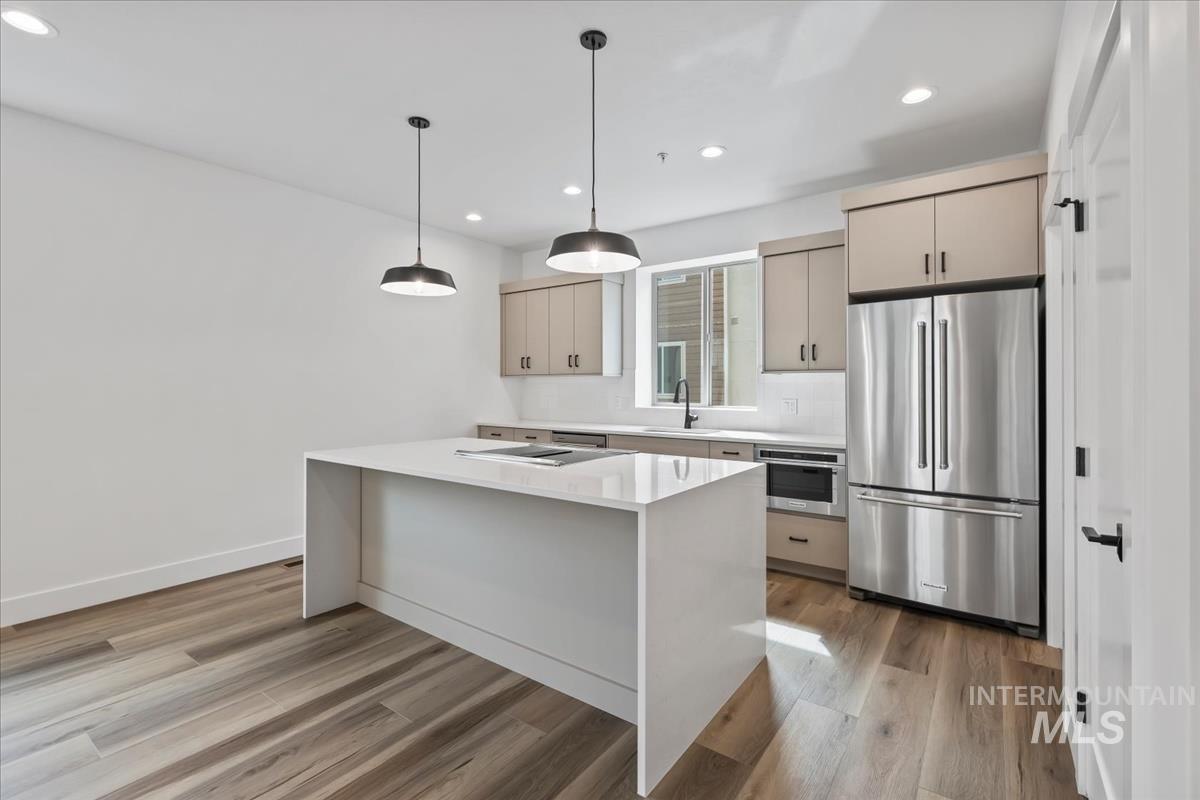 Kitchen with appliances with stainless steel finishes, light stone counters, hanging light fixtures, recessed lighting, and light wood finished floors