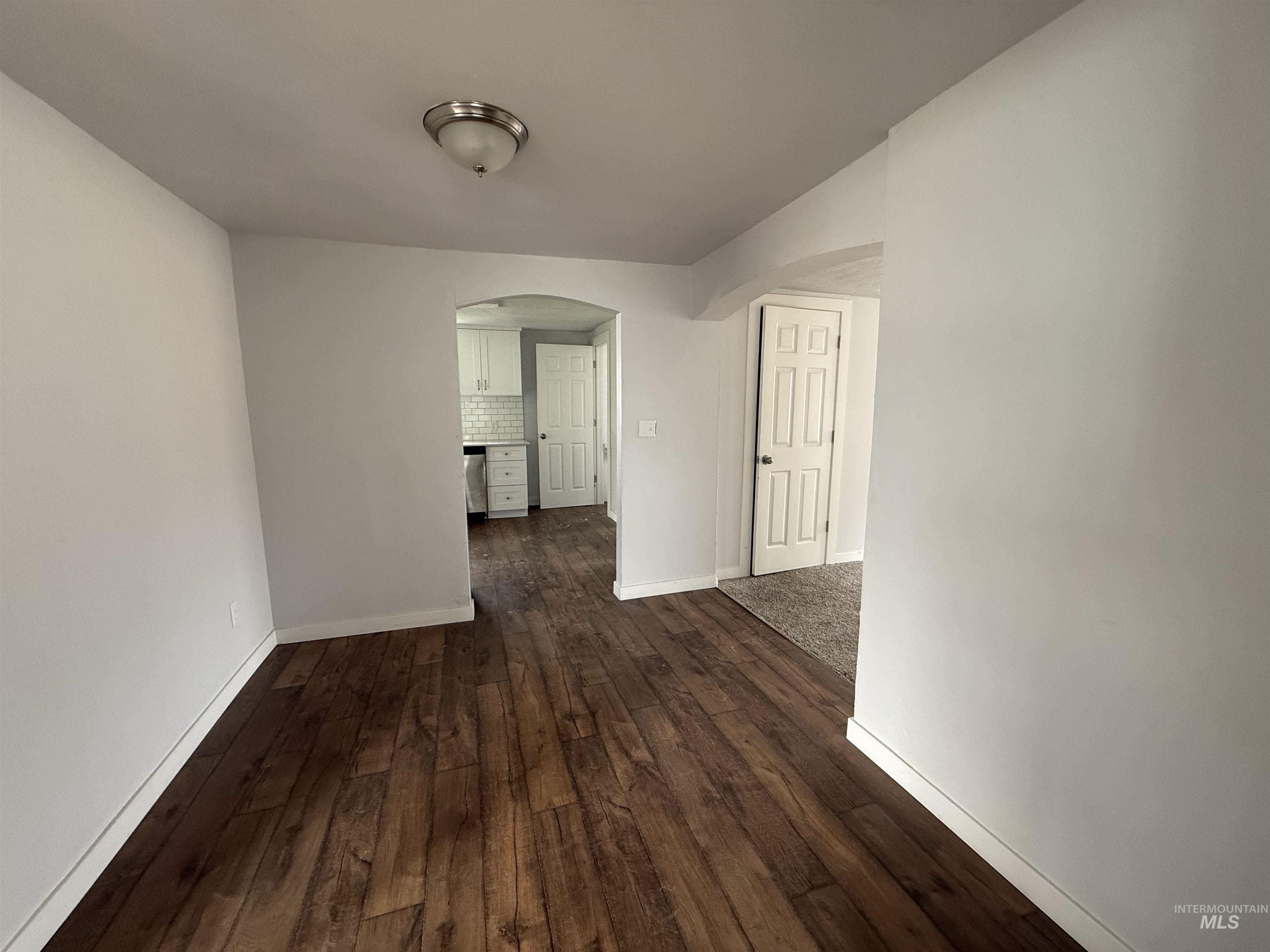 Unfurnished room featuring arched walkways and dark wood-style flooring