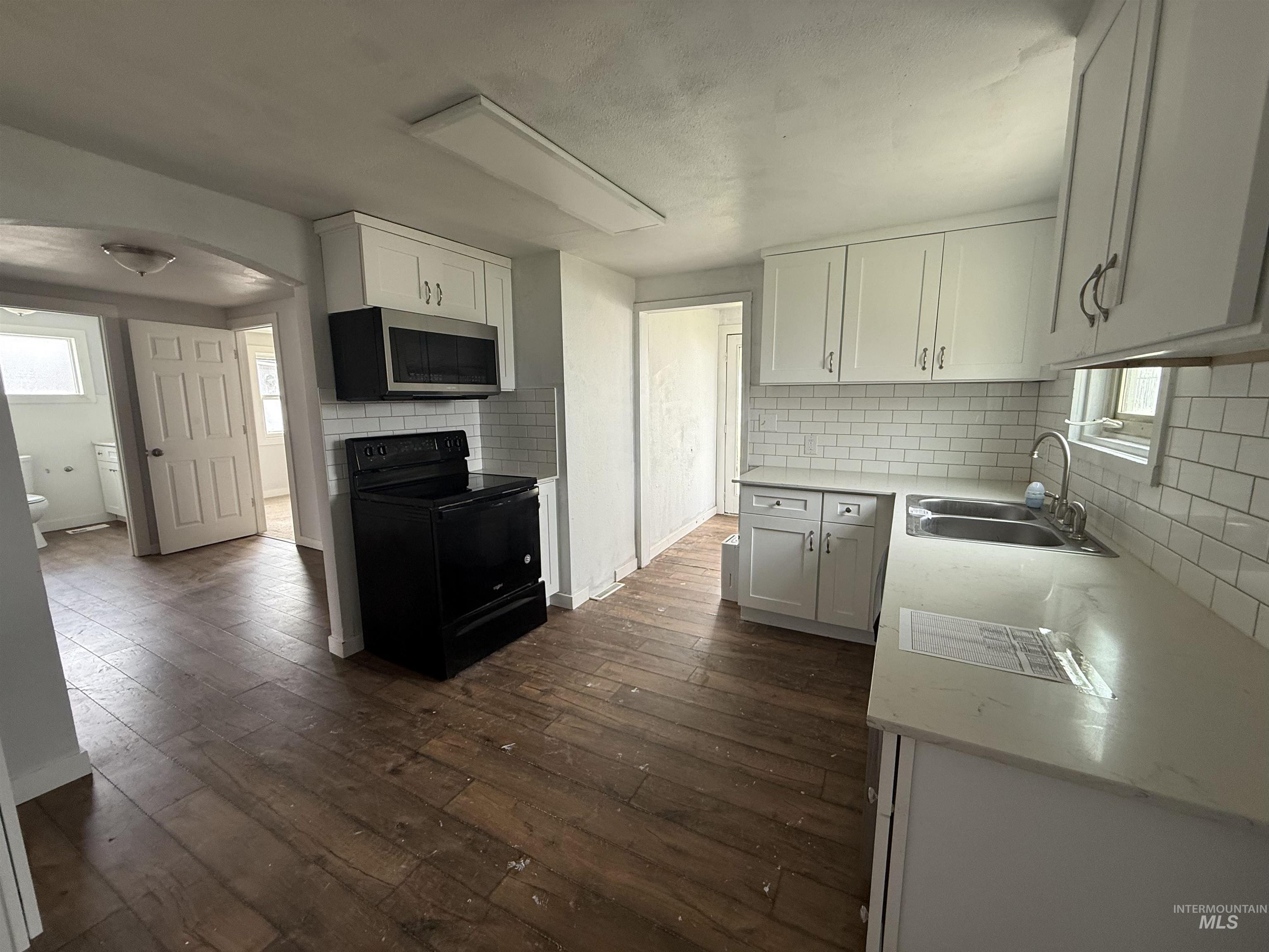 Kitchen featuring black range with electric cooktop, stainless steel microwave, white cabinetry, light stone counters, and dark wood-style flooring