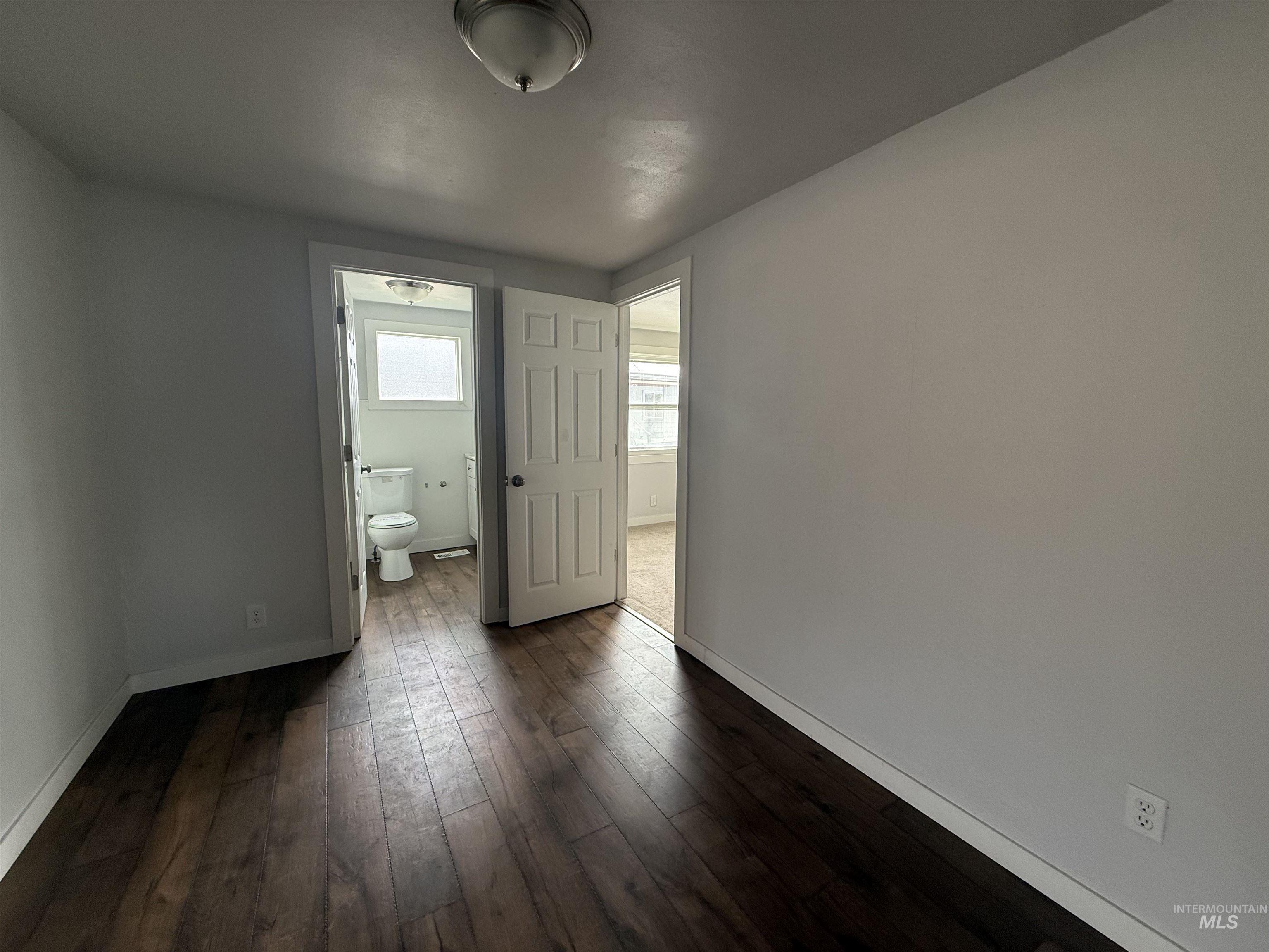 Unfurnished bedroom with dark wood finished floors and connected bathroom