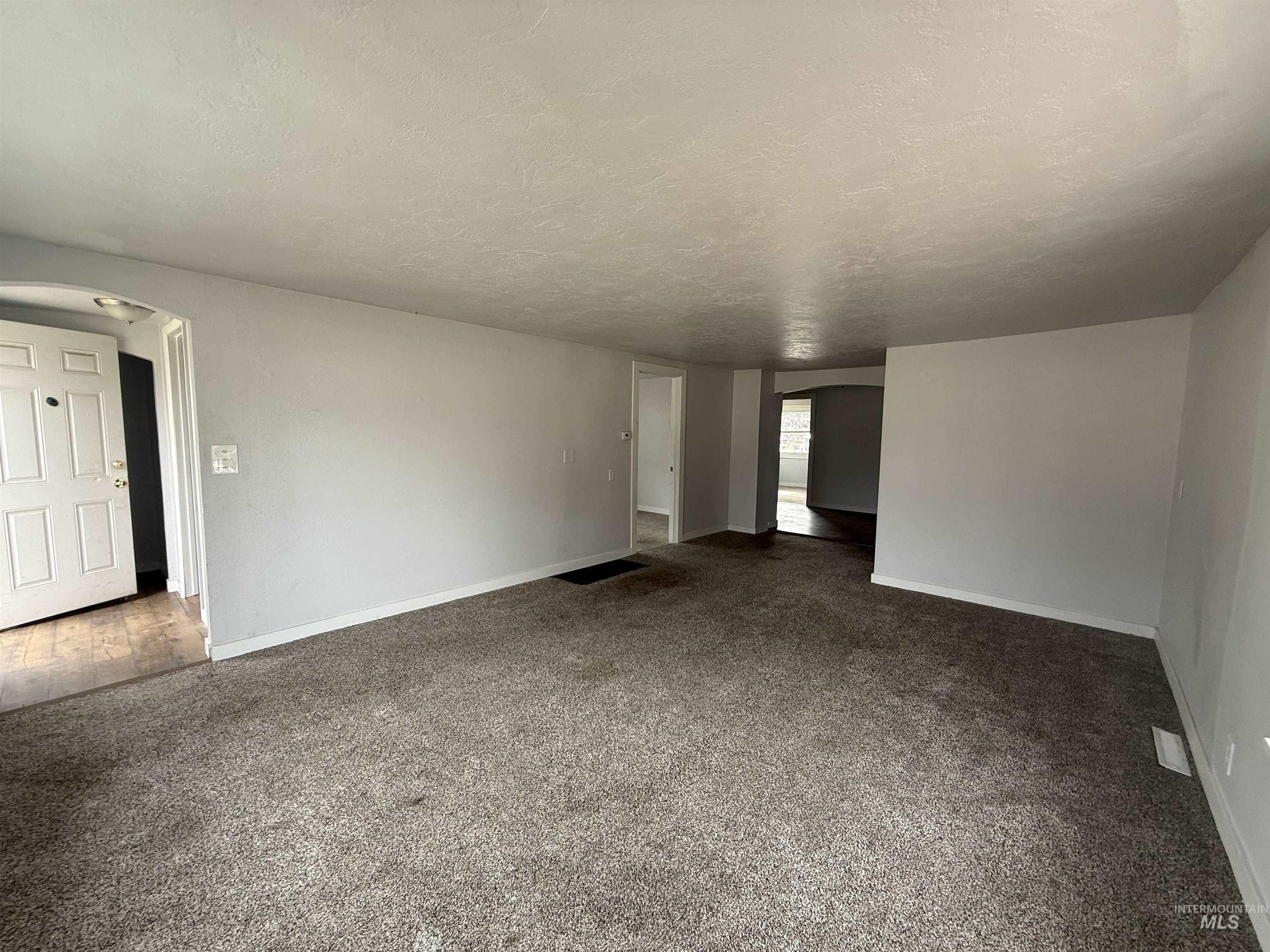 Carpeted empty room featuring arched walkways and a textured ceiling