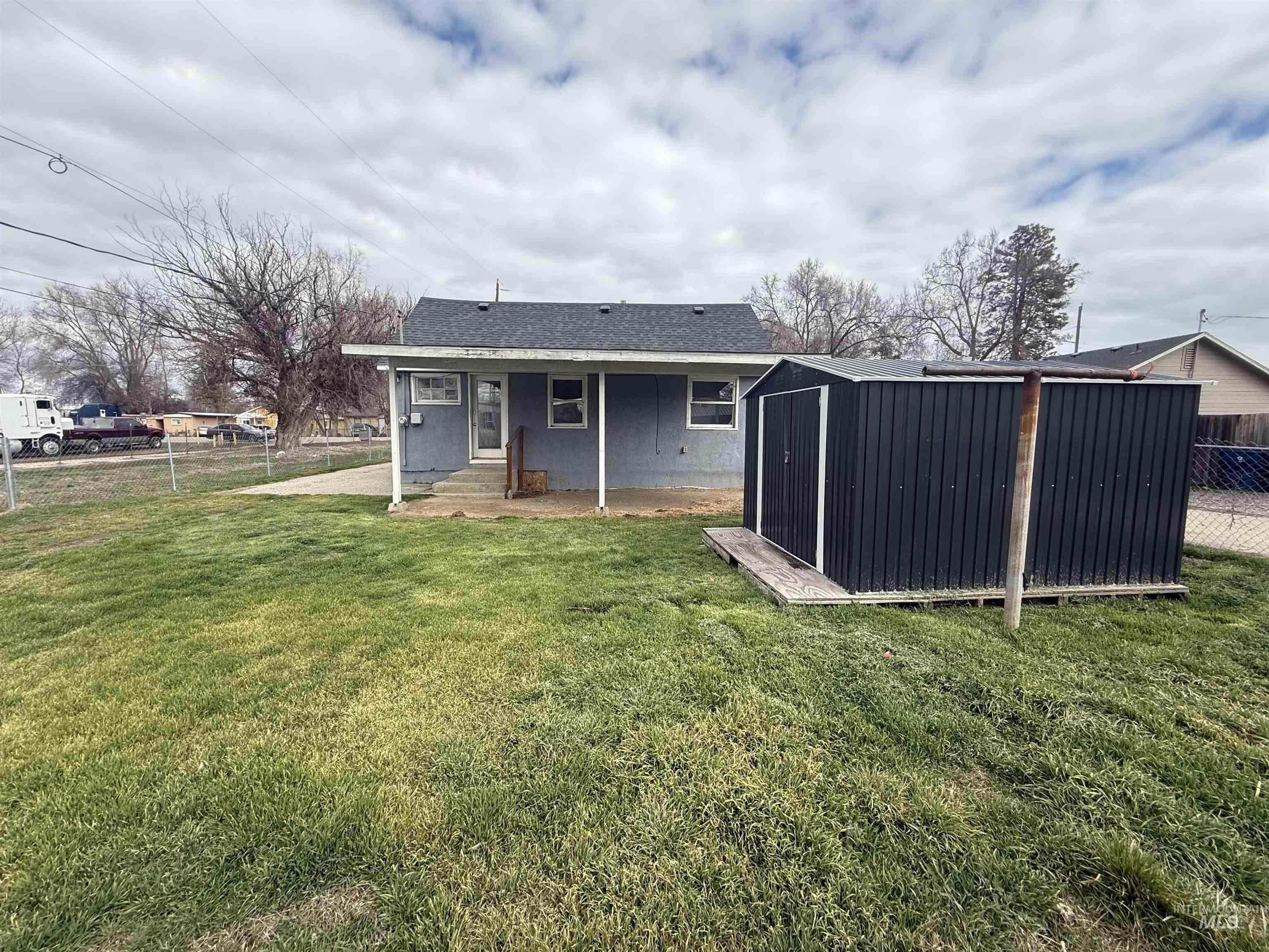 Rear view of property featuring roof with shingles, a storage shed, a fenced backyard, and a patio