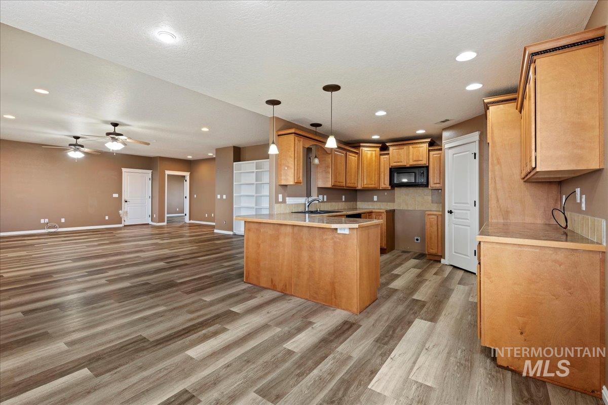 Kitchen with decorative light fixtures, a peninsula, open floor plan, light countertops, and ceiling fan
