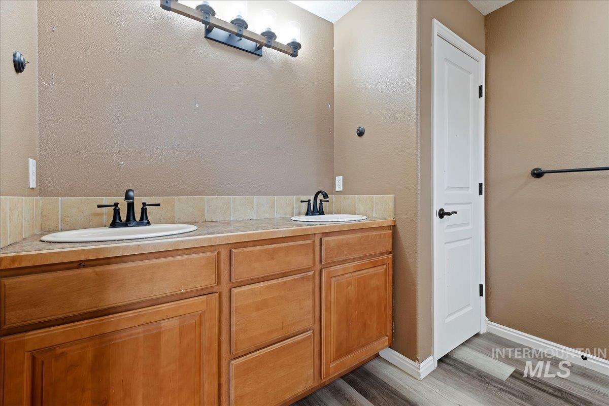 Full bath featuring double vanity, wood finished floors, and a textured wall