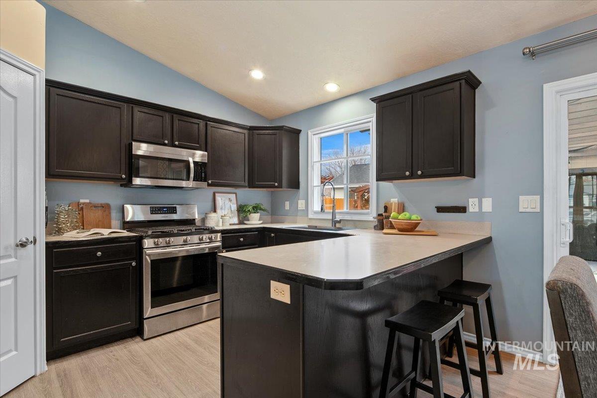 Kitchen with appliances with stainless steel finishes, lofted ceiling, a kitchen bar, light wood-style flooring, and recessed lighting