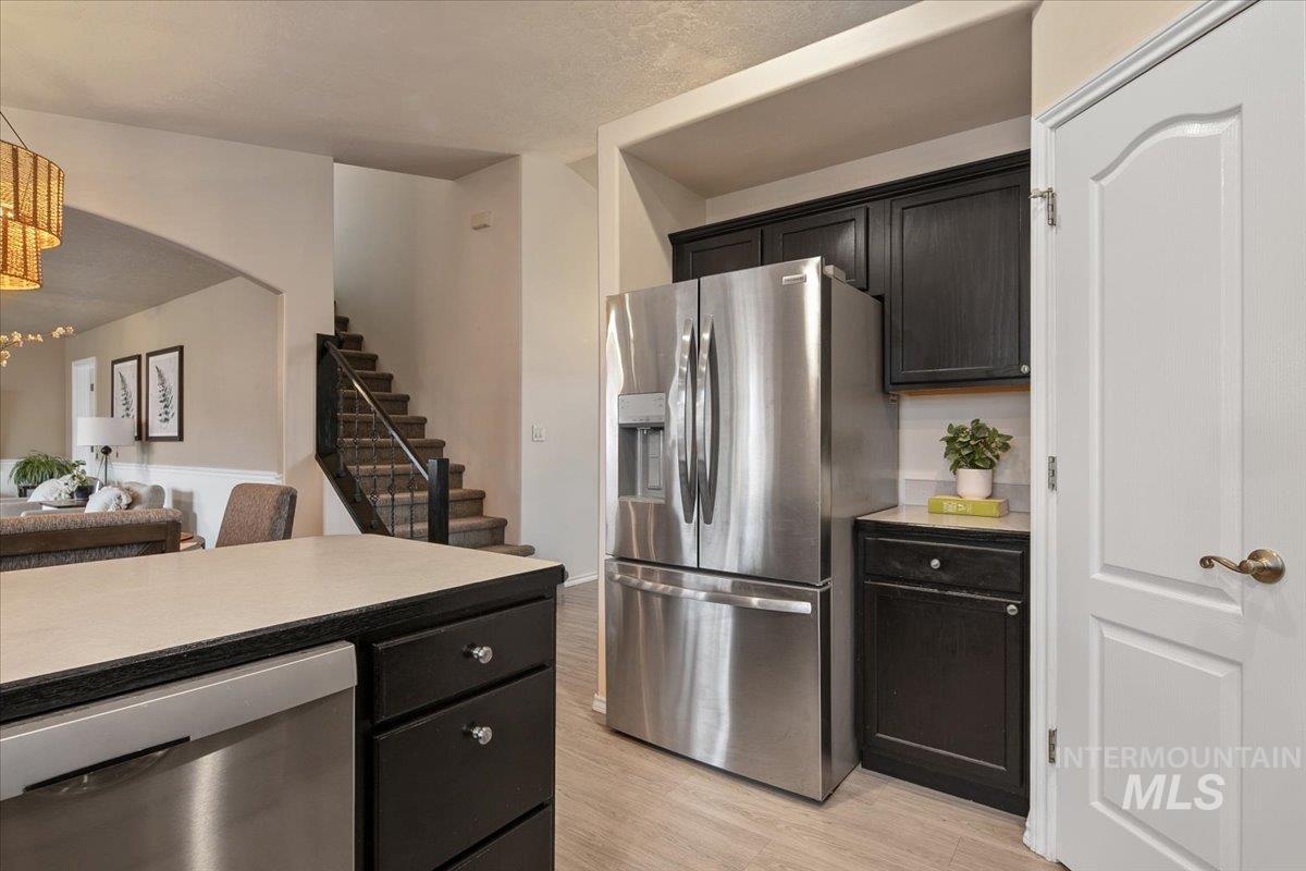 Kitchen with light countertops, appliances with stainless steel finishes, dark cabinets, light wood-type flooring, and open floor plan