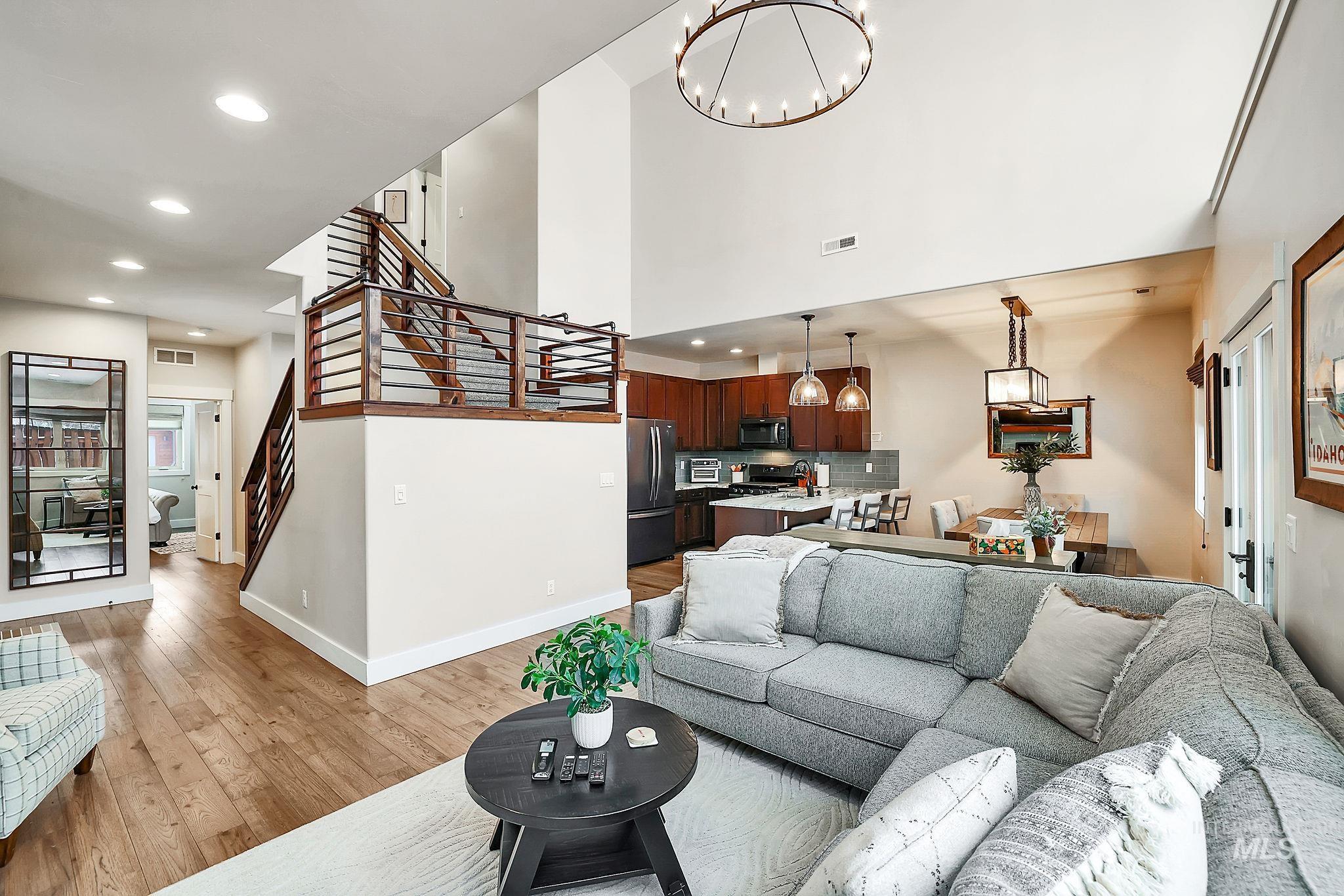 Living room with light wood-style floors, hanging lights, and a high ceiling