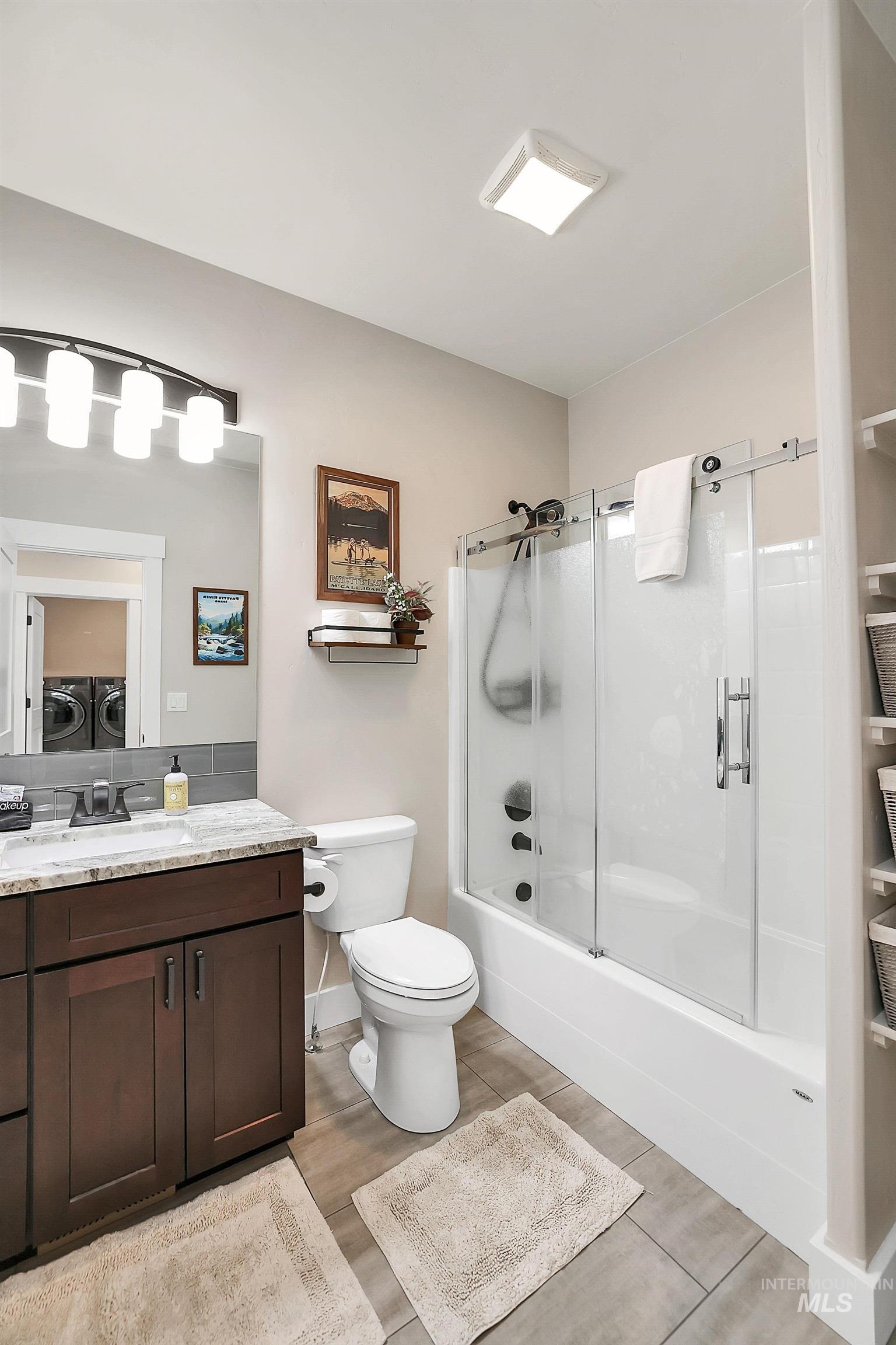 Bathroom featuring vanity, light wood finished floors, shower / bath combination with glass door, and separate washer and dryer