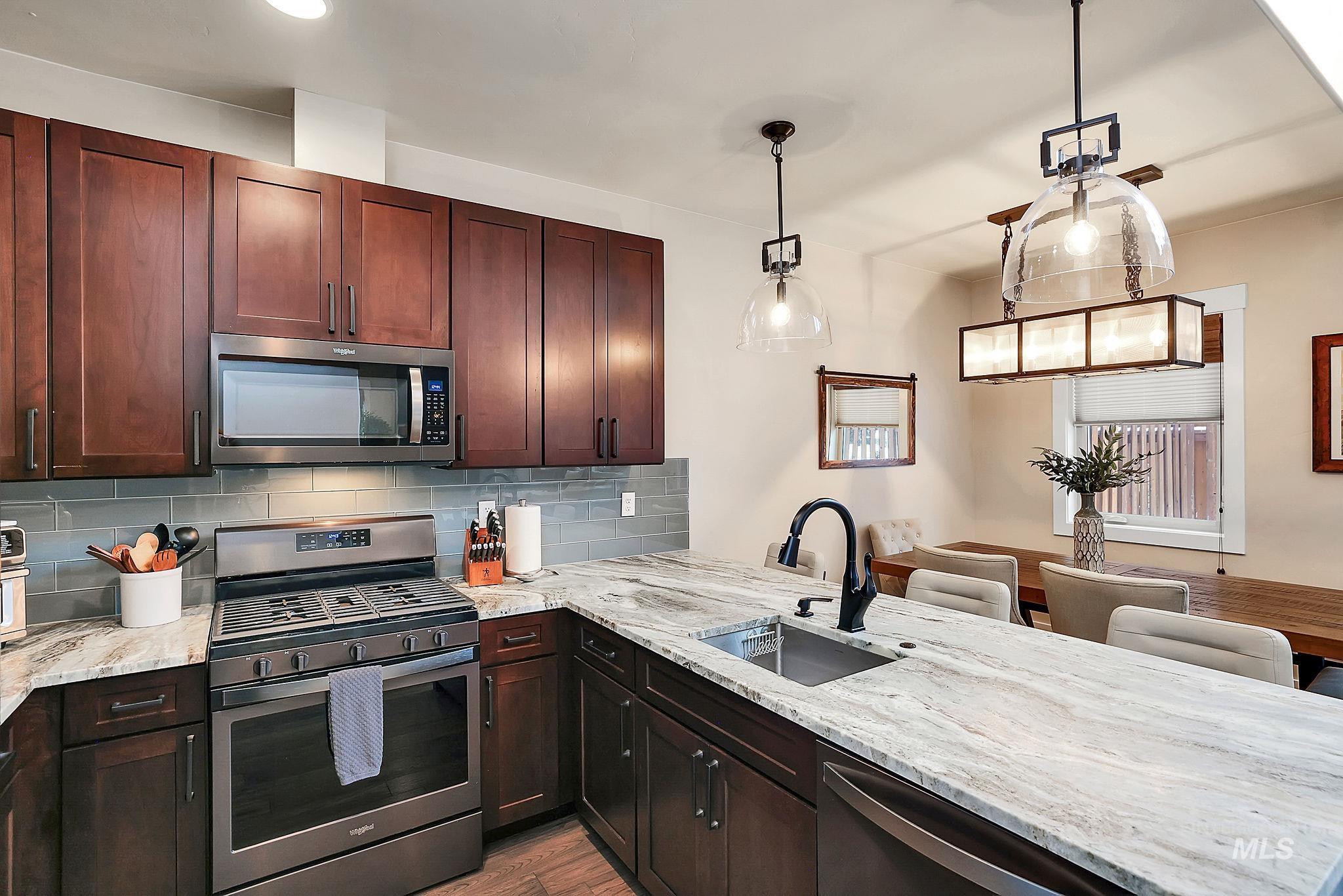 Kitchen with stainless steel appliances, light stone countertops, hanging light fixtures, a peninsula, and tasteful backsplash