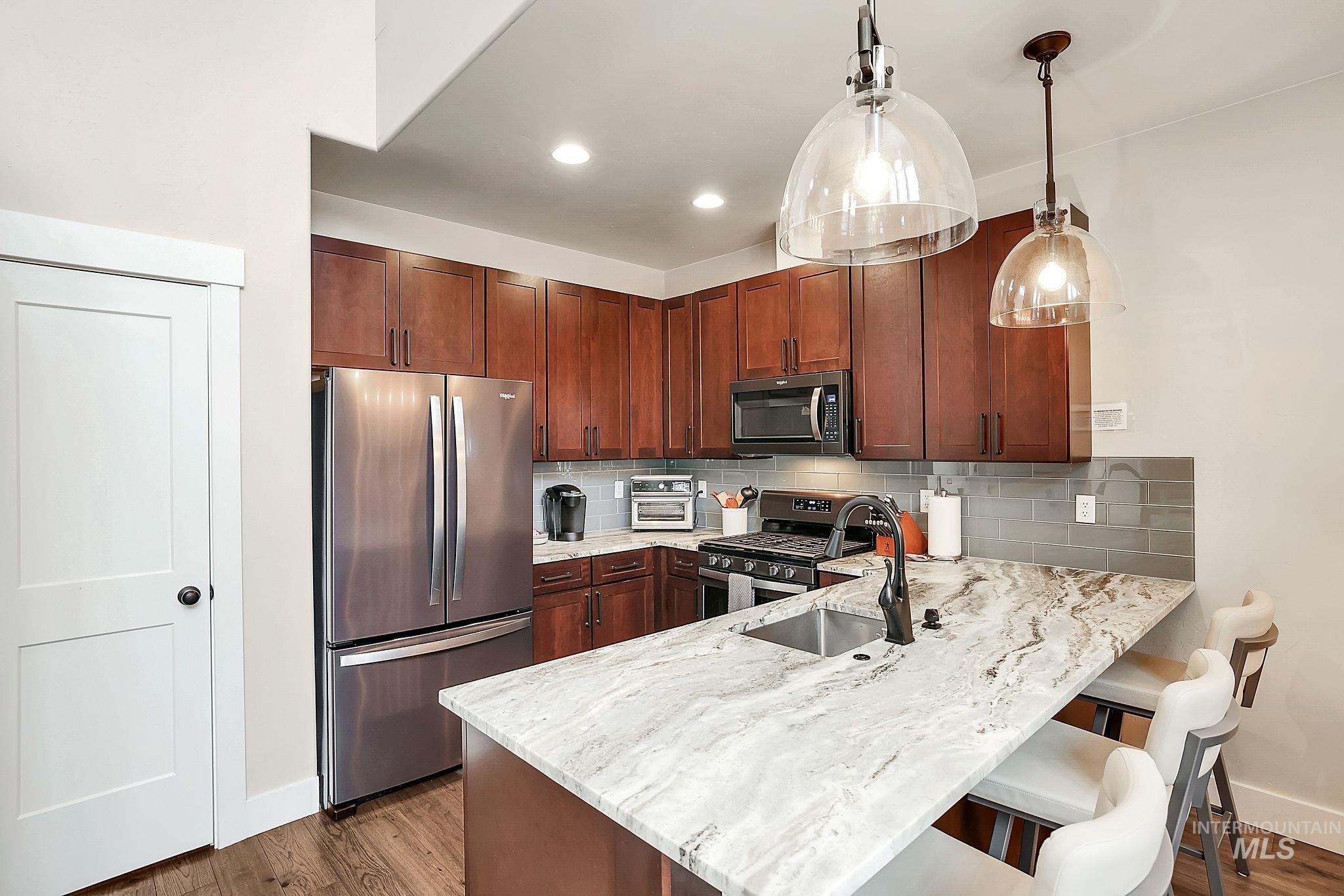 Kitchen featuring stainless steel appliances, pendant lighting, light stone counters, a breakfast bar area, and a peninsula