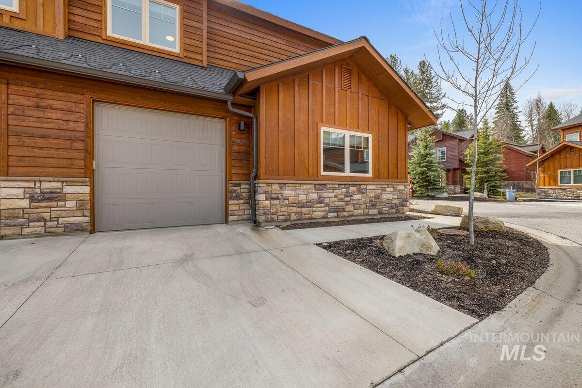 View of front of house featuring stone siding, driveway, board and batten siding, a garage, and a shingled roof