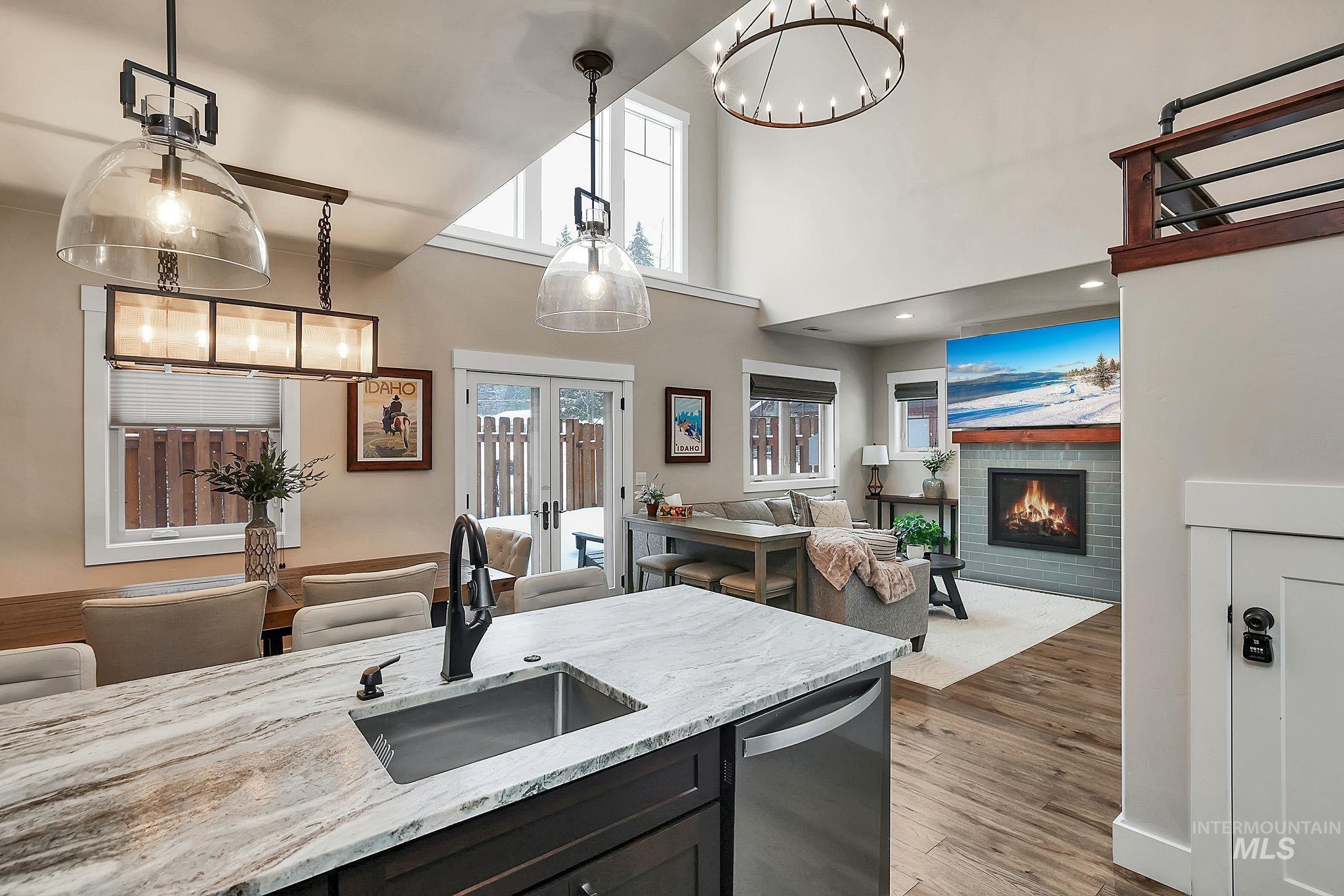 Kitchen with light stone counters, light wood finished floors, dishwasher, a lit fireplace, and suspended lighting