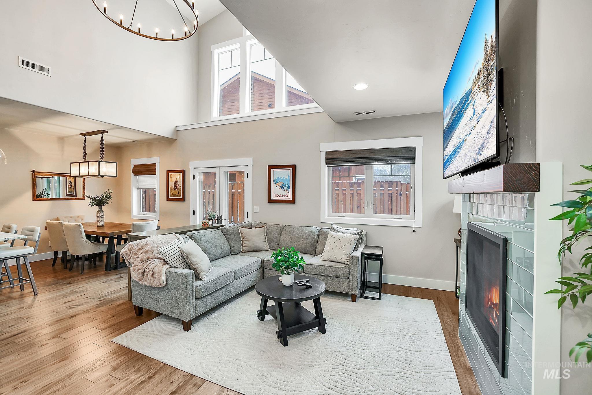 Living area with a chandelier, a warm lit fireplace, light wood finished floors, and a high ceiling