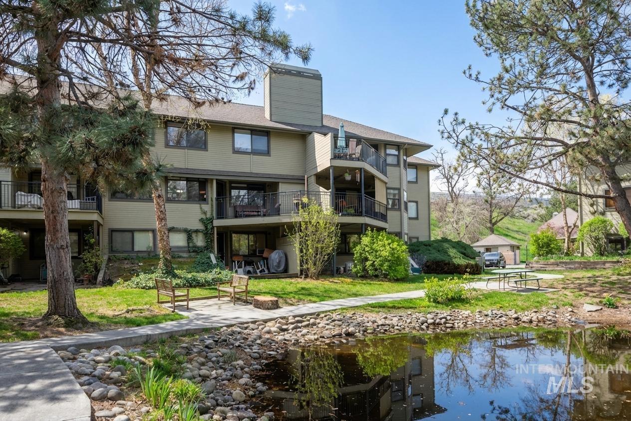 Rear view of house featuring a chimney, an outdoor fire pit, a water view, a balcony, and a lawn