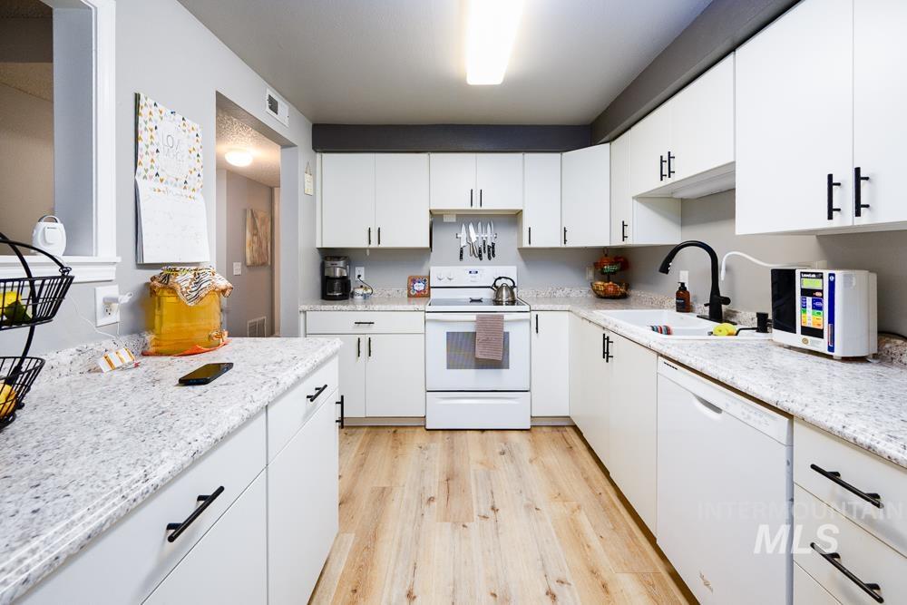Kitchen with white appliances, light wood-style floors, white cabinets, and light stone counters