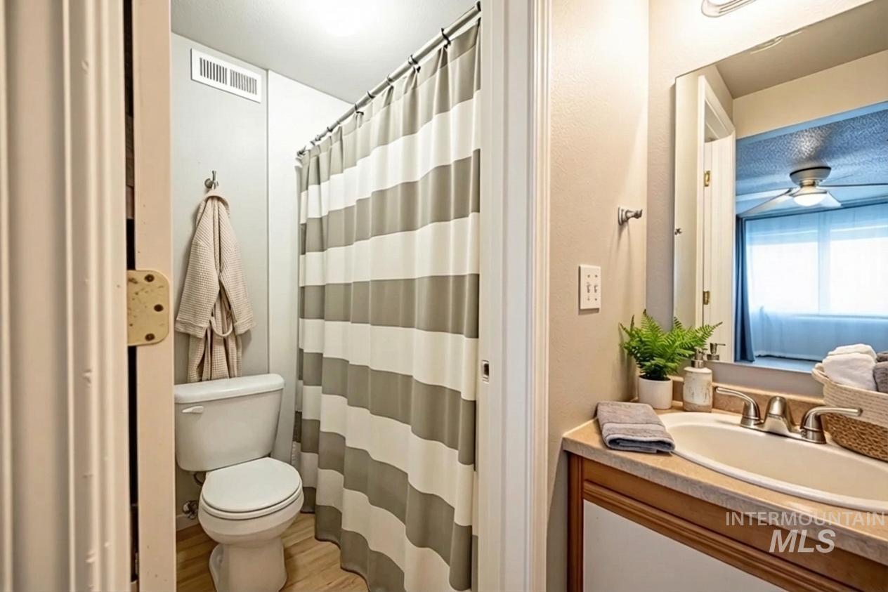 Bathroom with a shower with curtain, vanity, light wood-style flooring, and ceiling fan
